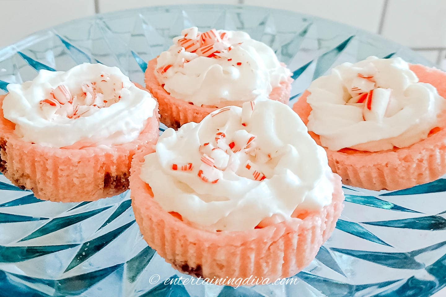 Peppermint cheesecake cupcakes topped with crushed candy canes on a serving tray