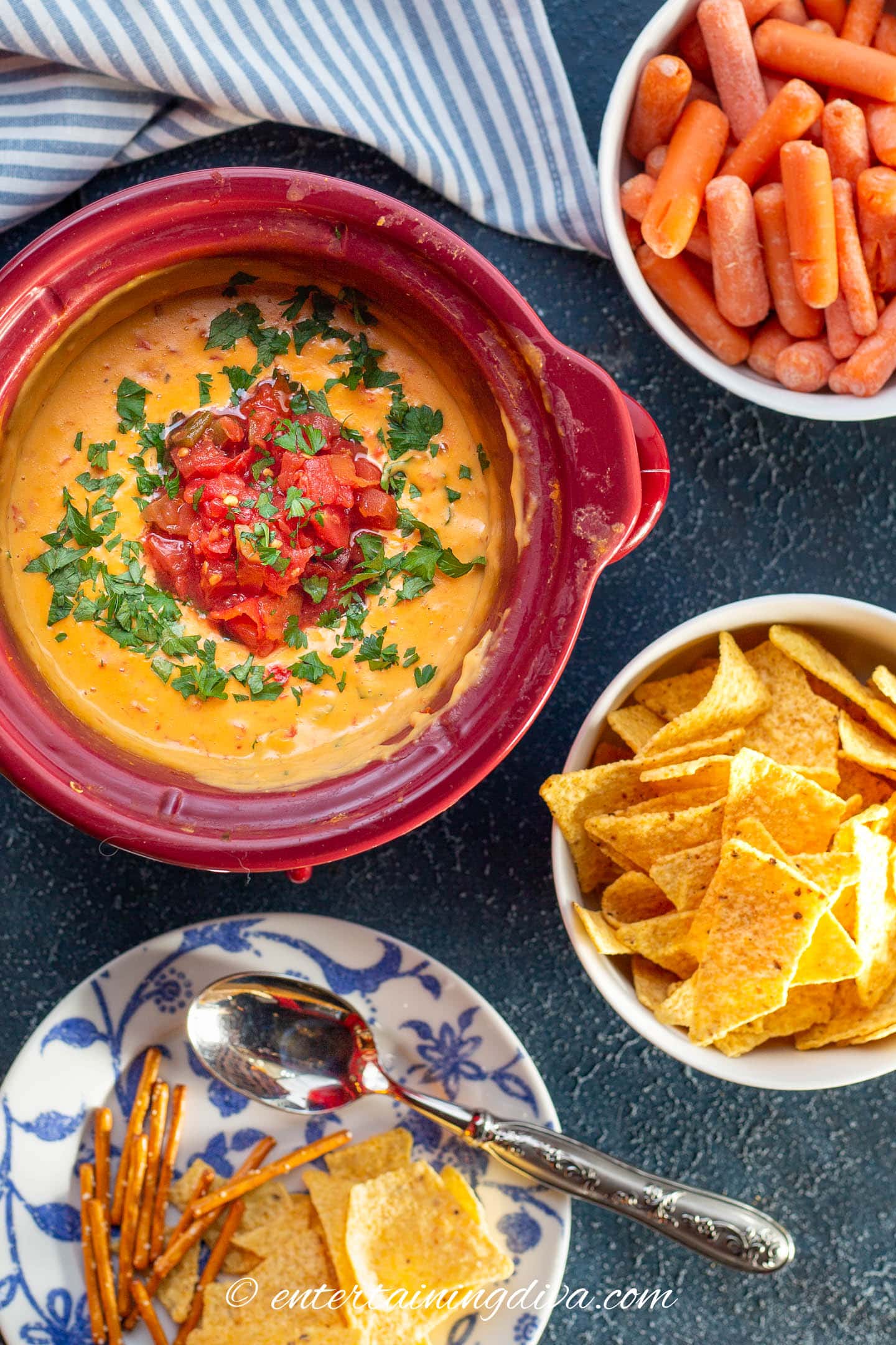Velveeta Rotel cheese dip in a crock pot served with bowls of carrots, tortilla chips and pretzels