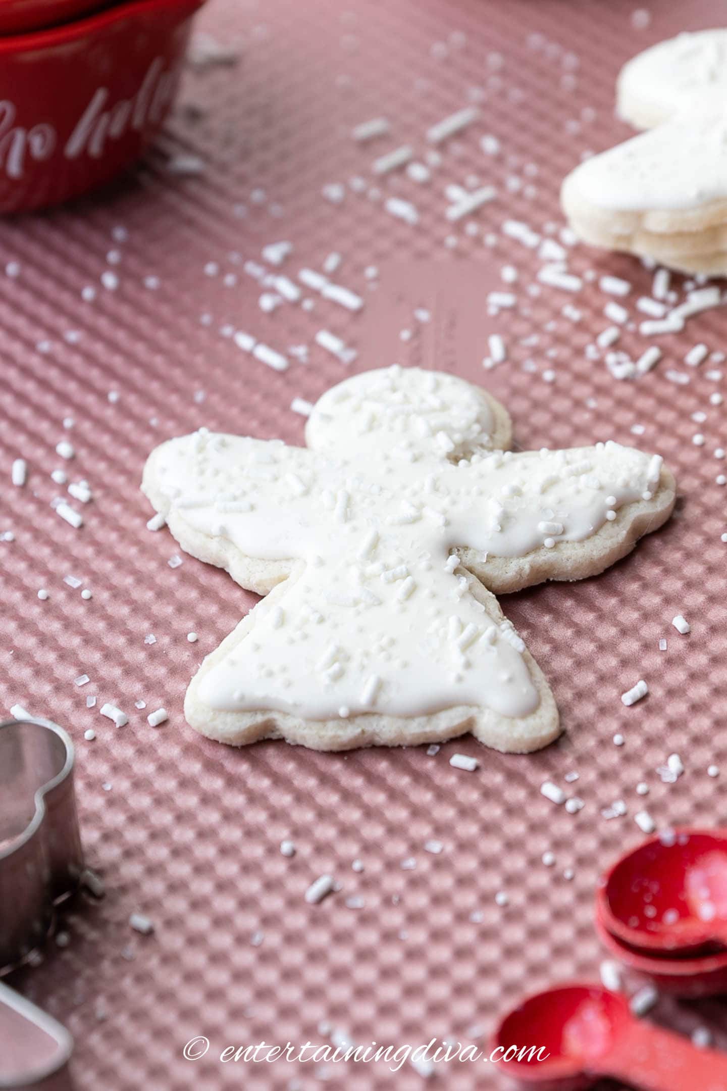Christmas angel cutout cookie decorated with white royal icing and white sprinkles on a baking sheet