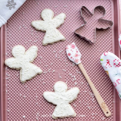 Decorated Christmas angel rolled sugar cookies on a baking sheet with an angel cookie cutter and a spatula