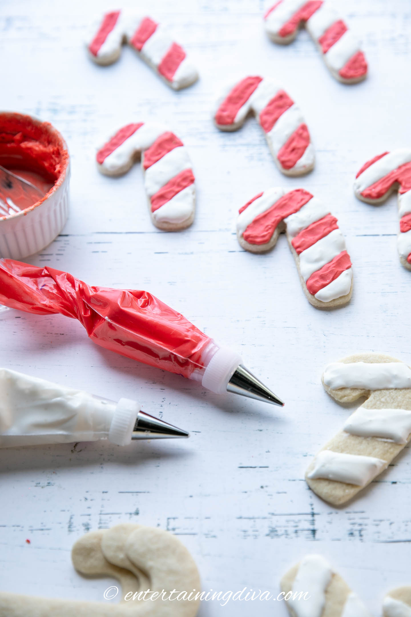 Candy cane sugar cookies with red and white royal icing in piping bags