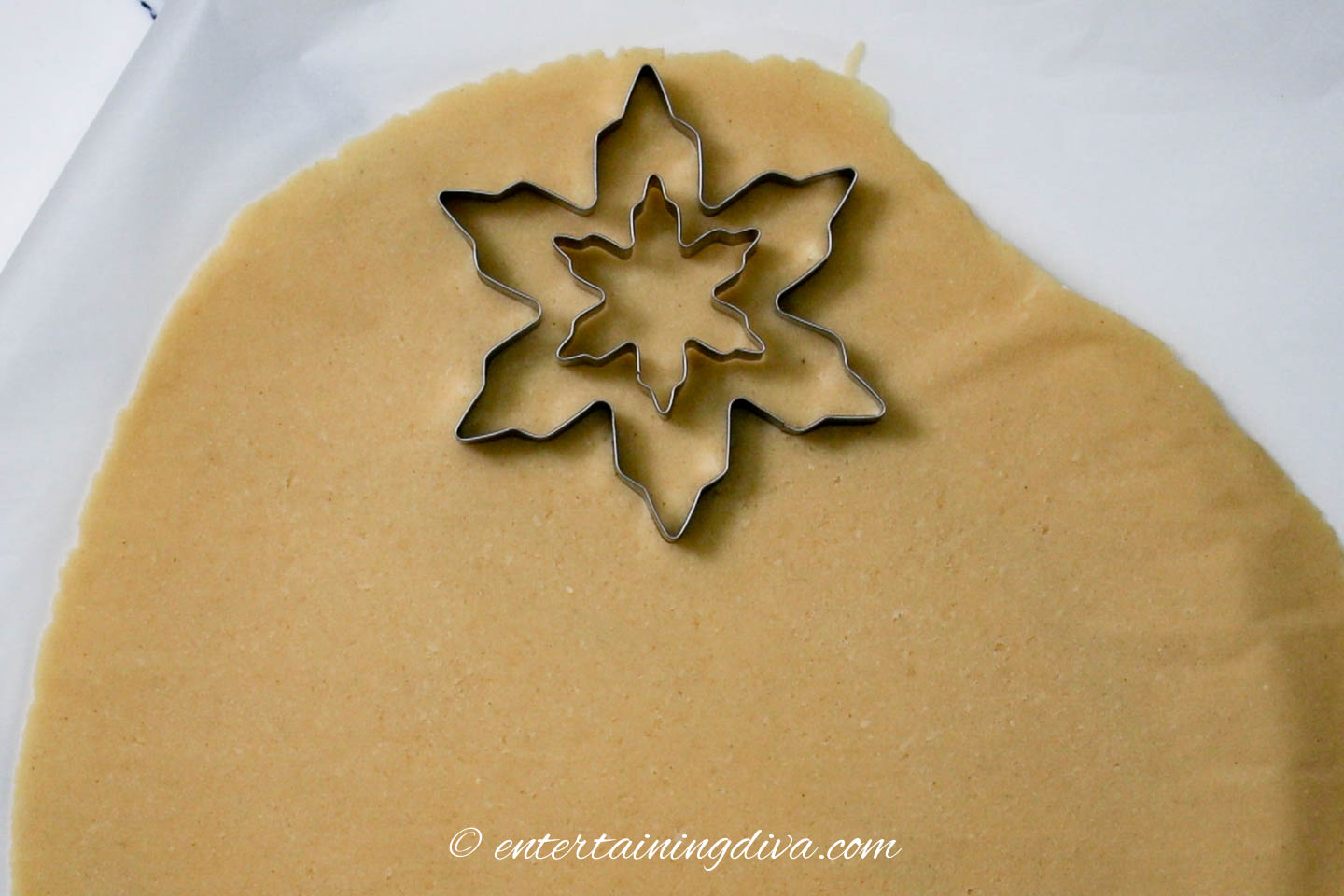 large and small snowflake cookie cutters on rolled out cookie dough