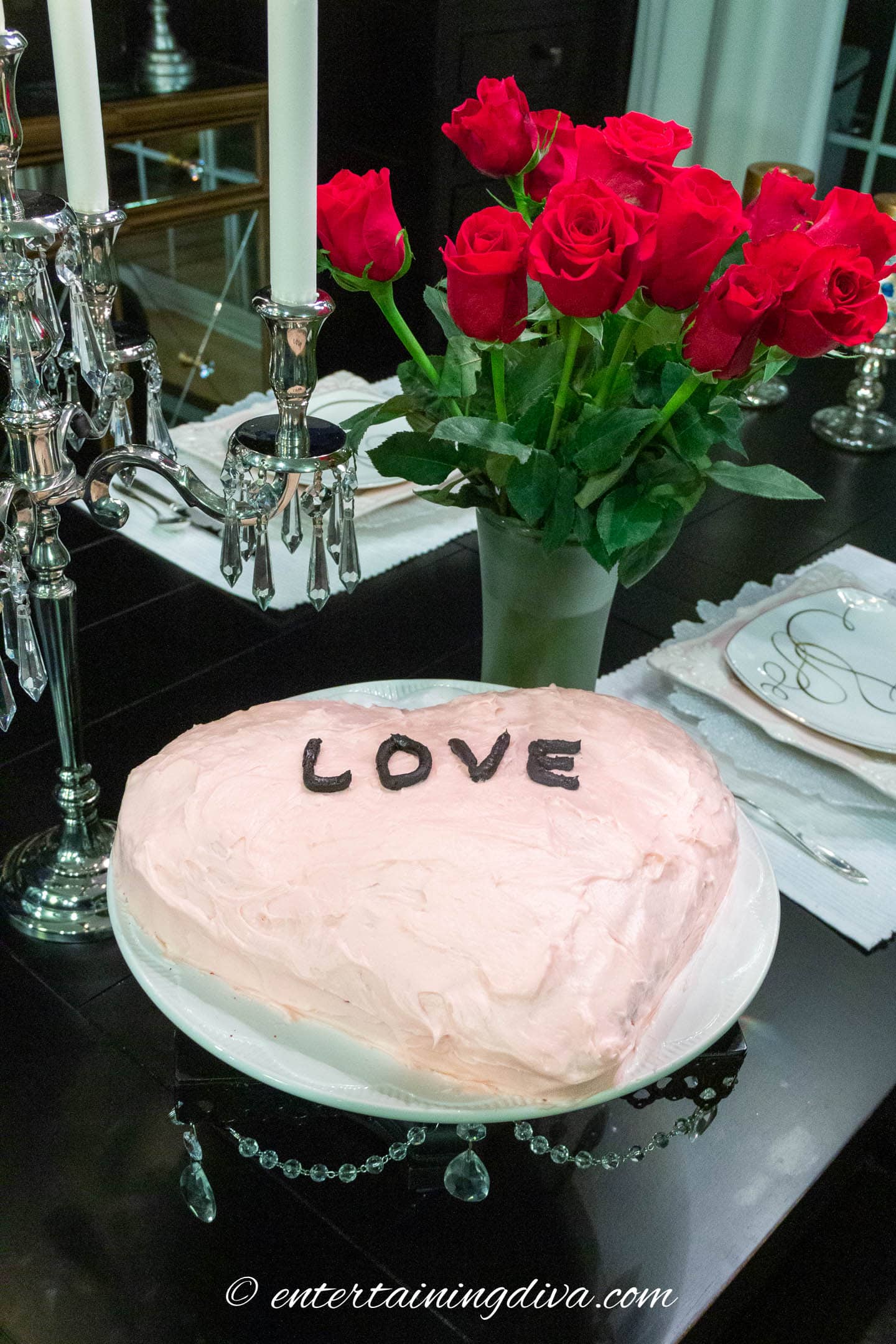 Valentine's Day table with red roses and pink cake with the word LOVE on it