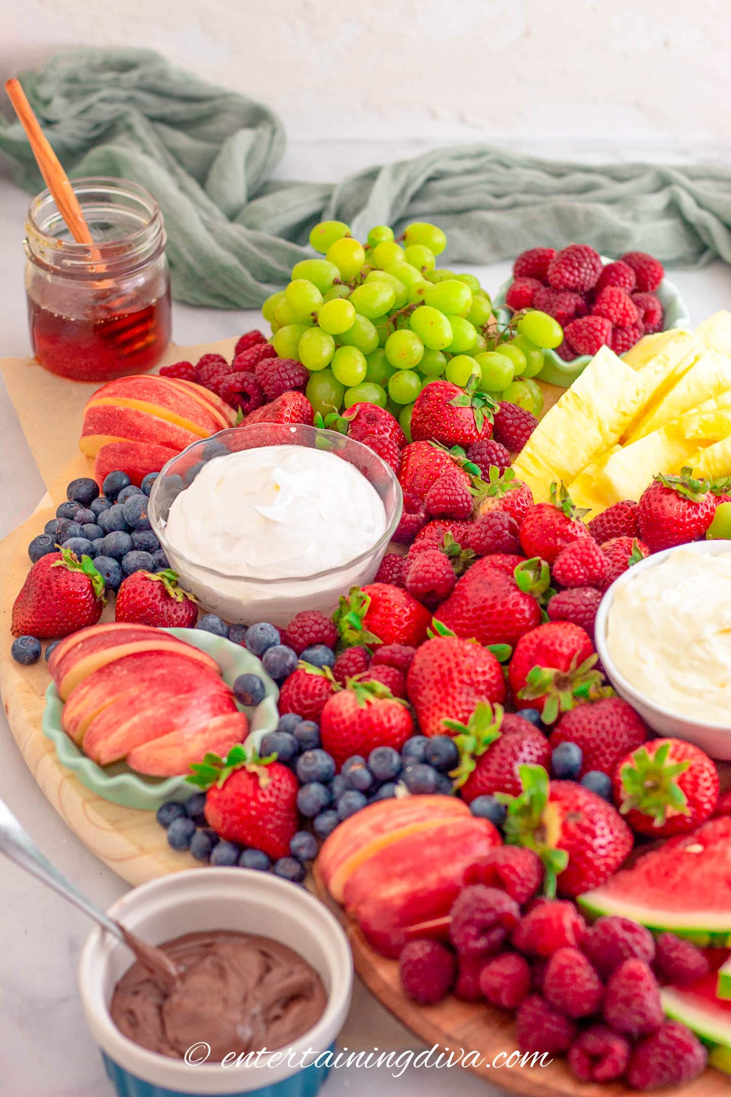 angled view of a fresh fruit charcuterie board with strawberries, blueberries, raspberries, grapes, apples, pineapple, watermelon and various dips