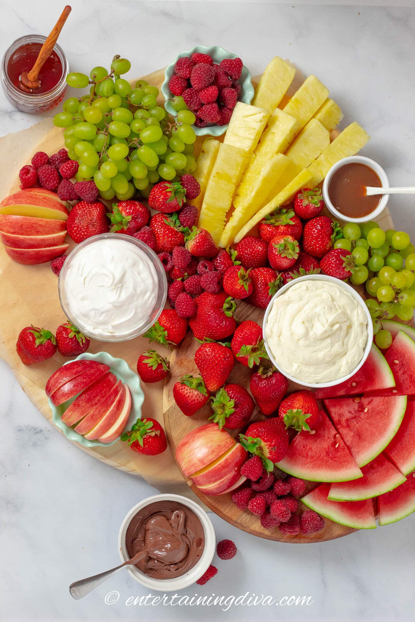 fruit charcuterie board with raspberries, strawberries, apples, pineapple, grapes, watermelon and dips.