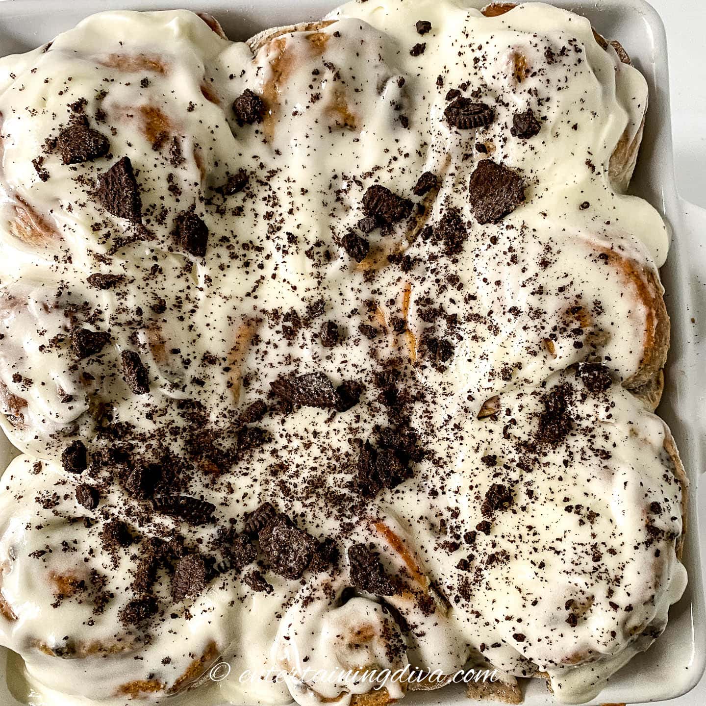 a pan of cinnamon rolls with glaze and Oreo cookies on top