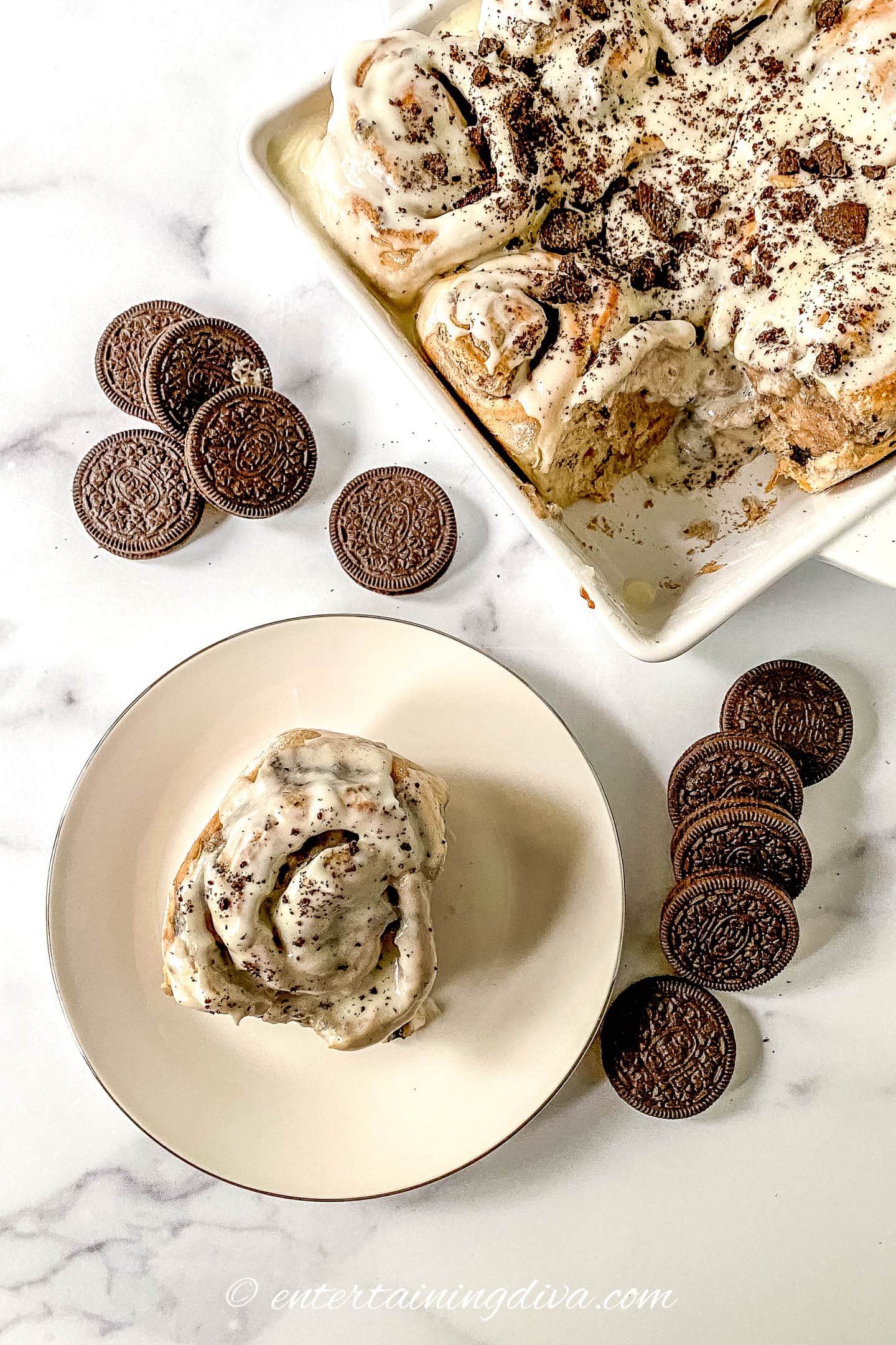 Overhead picture of an Oreo cinnamon roll on a plate beside a pan of cinnamon rolls with Oreo cookies on the icing