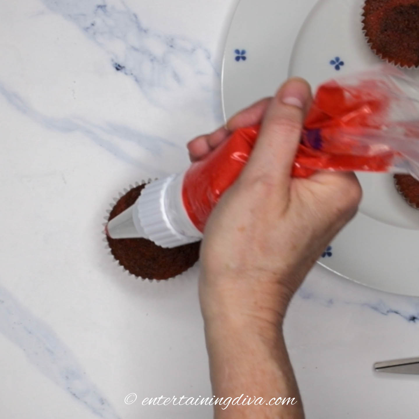 piping bag with red icing being held above a cupcake