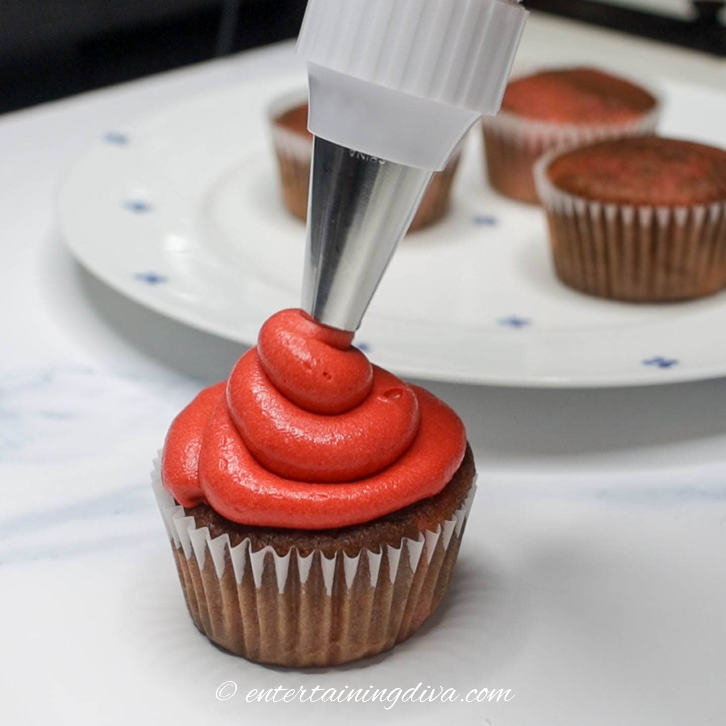 Red icing being piped onto a cupcake