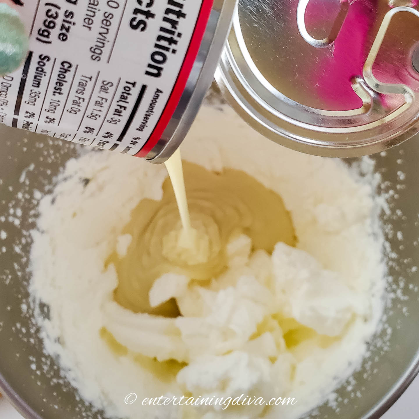 sweetened condense milk being poured into a bowl of whipped cream