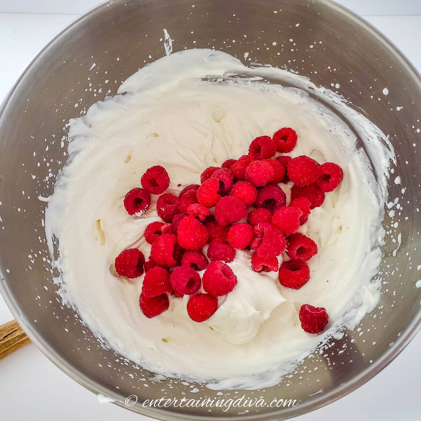 raspberries on top of whipped cream and sweetened condensed milk in a bowl