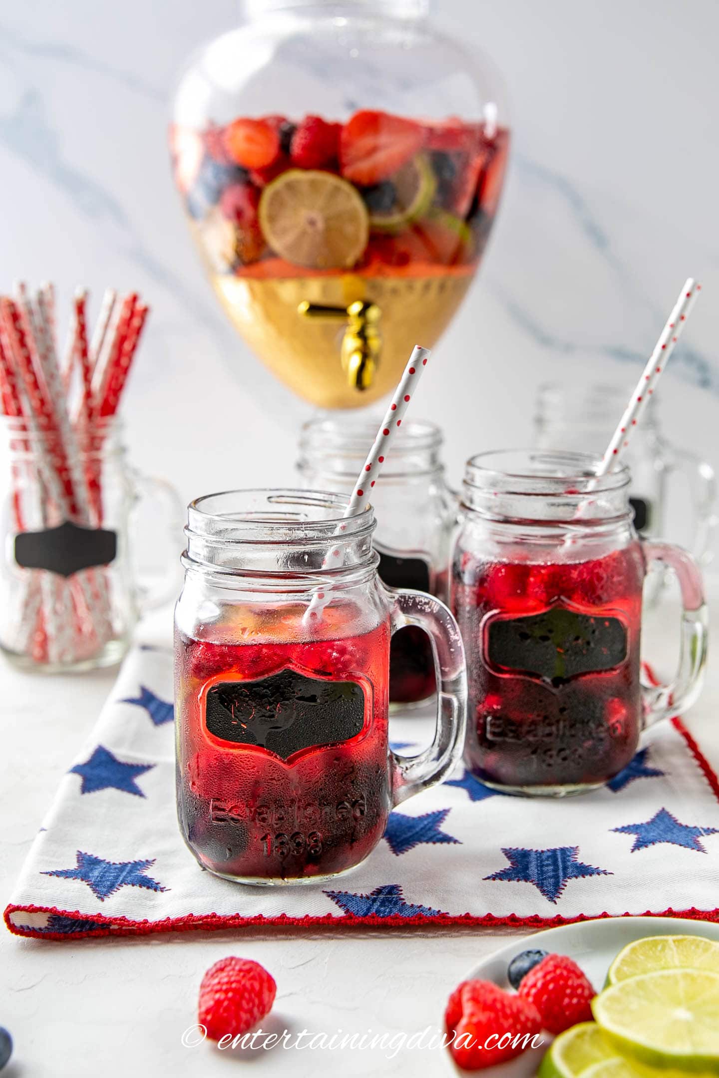 berries and lime sangria in mason jar glasses in front a drink dispenser