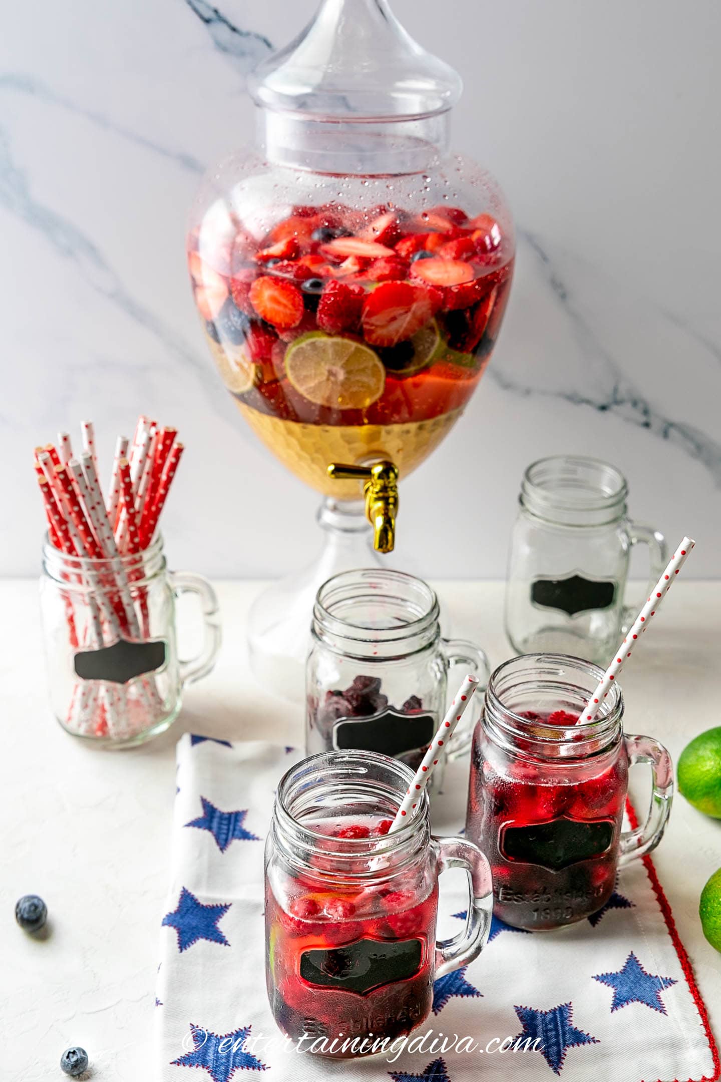 berries and lime sangria in a drink dispenser with mason jar glasses and straws