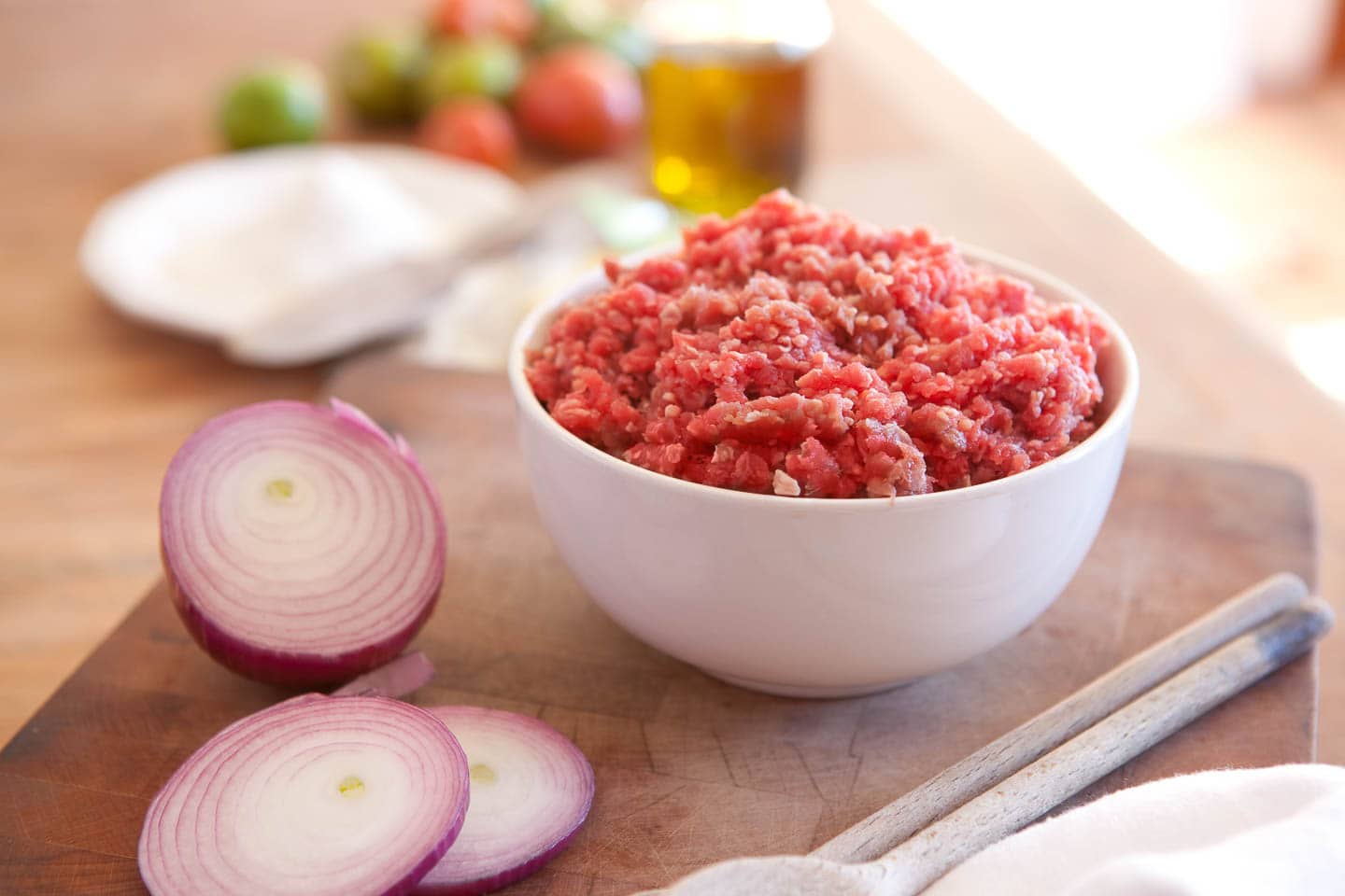 raw ground beef in a bowl with onions beside it and other nacho ingredients in the background