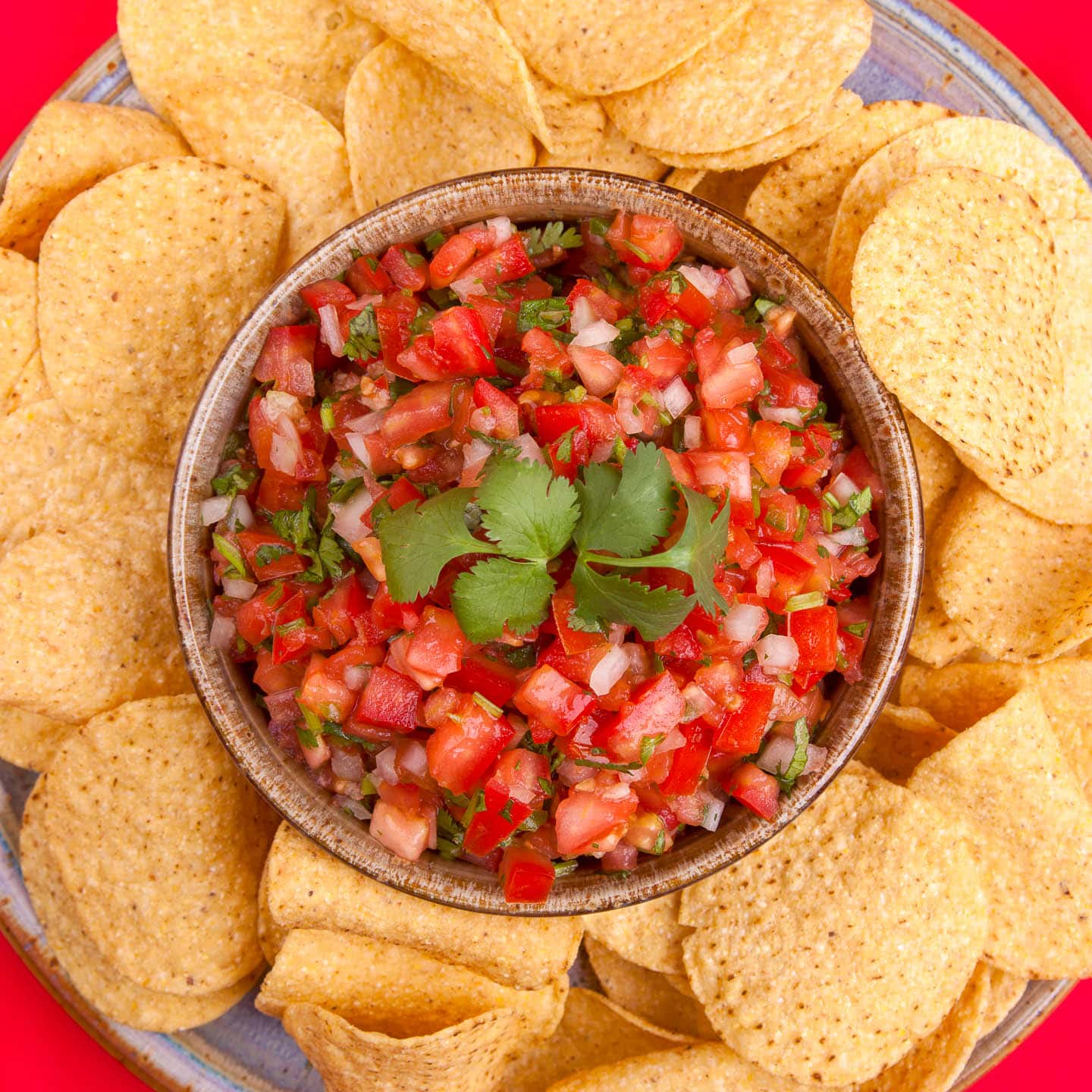 overhead picture of pico de gallo in a bowl surrounded by chips on a plate