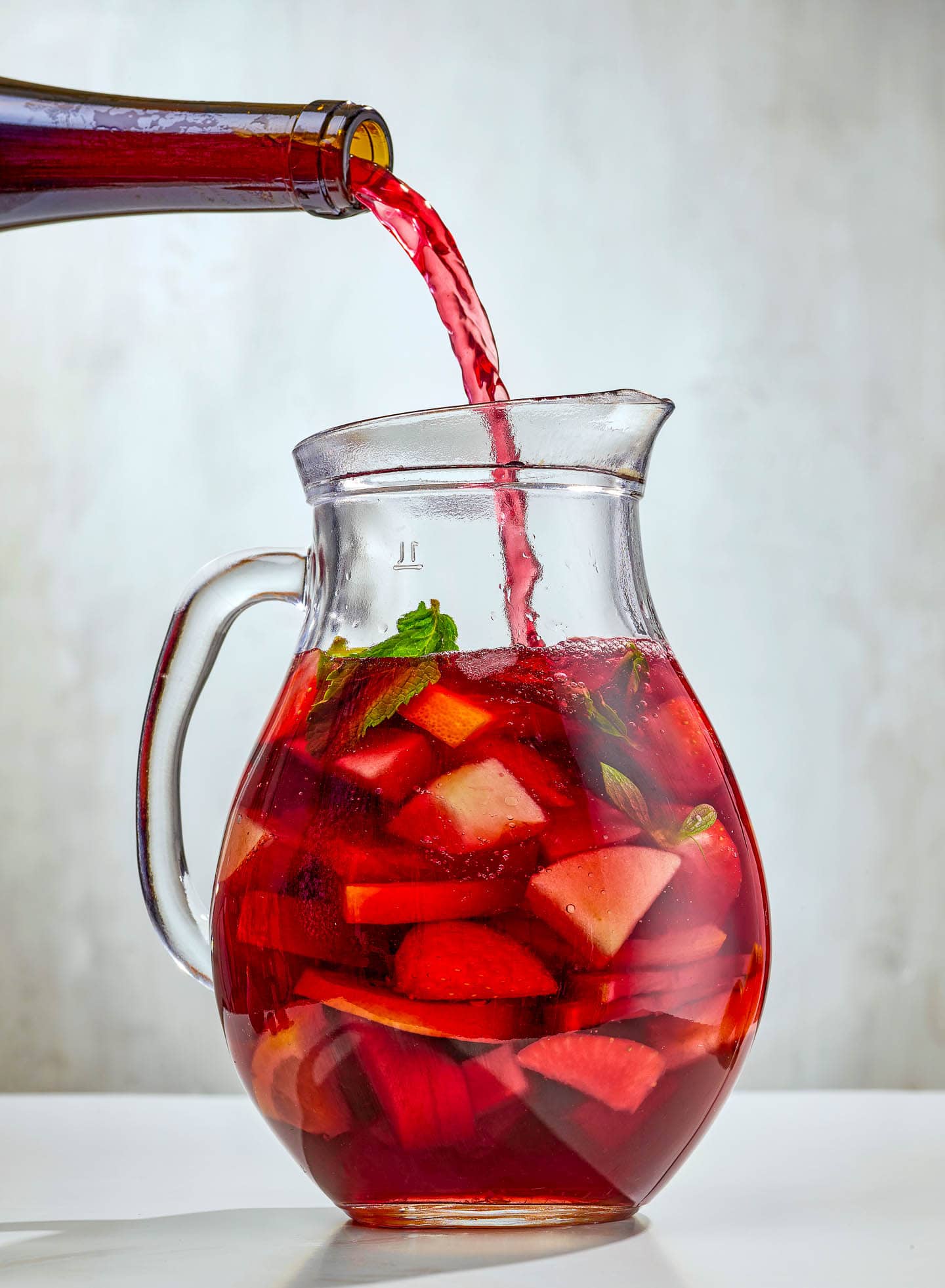 red wine being poured into a pitcher of sangria