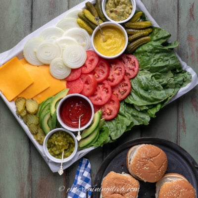 burger toppings charcuterie board beside a plate of hamburgers