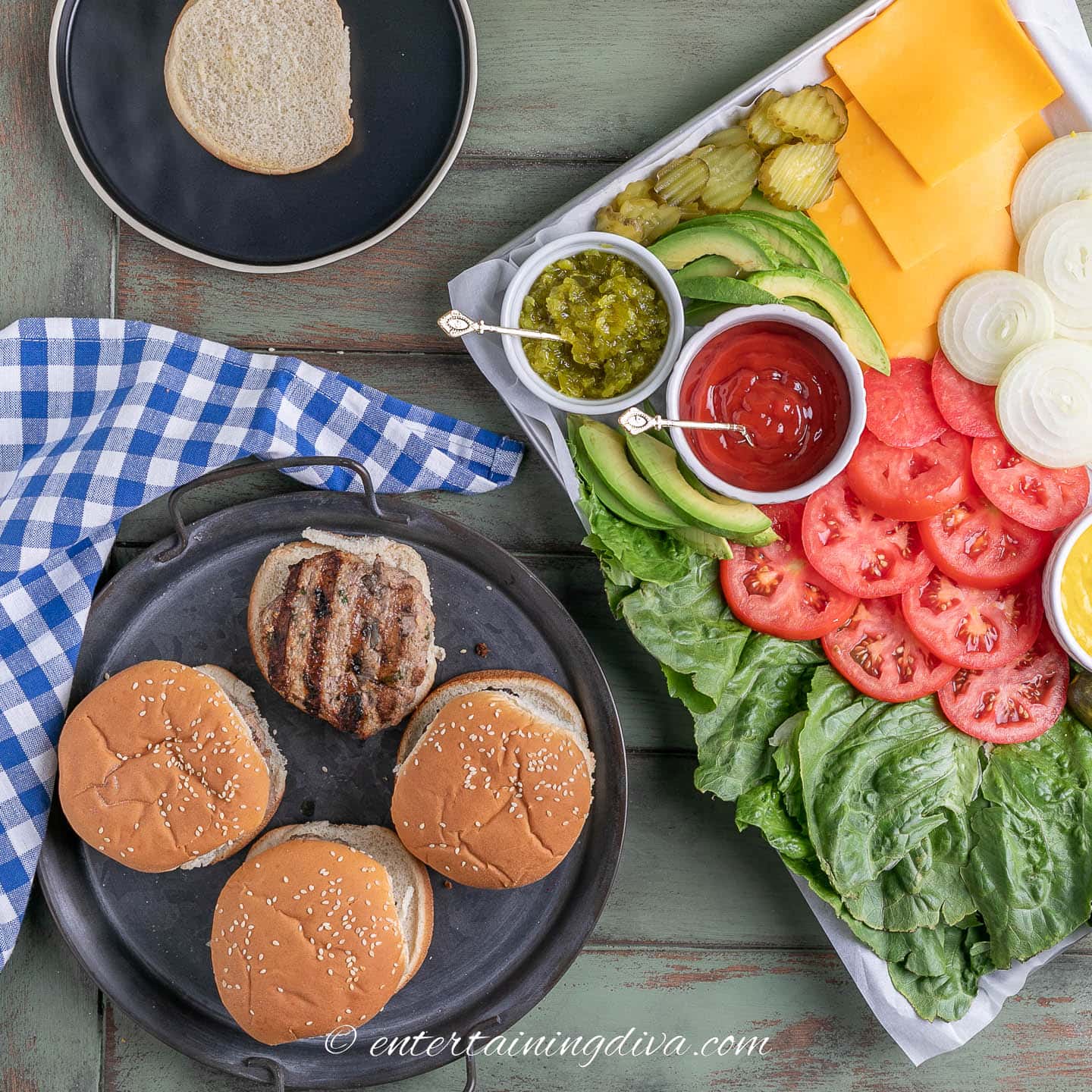 4 turkey burgers on a tray beside a burger topping charcuterie board
