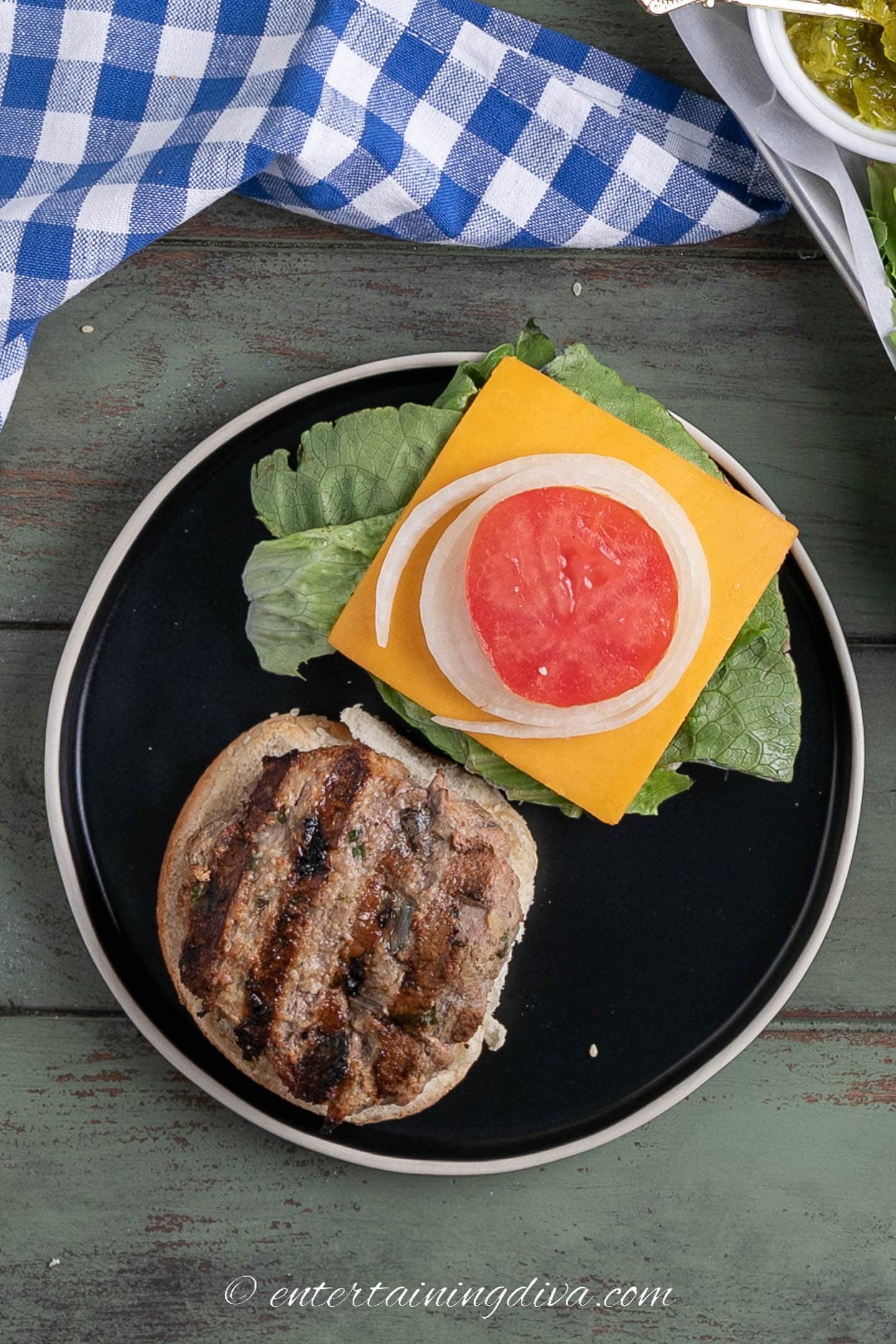 A grilled pesto turkey burger with the bun opened and lettuce, cheese, tomato and onion on it.
