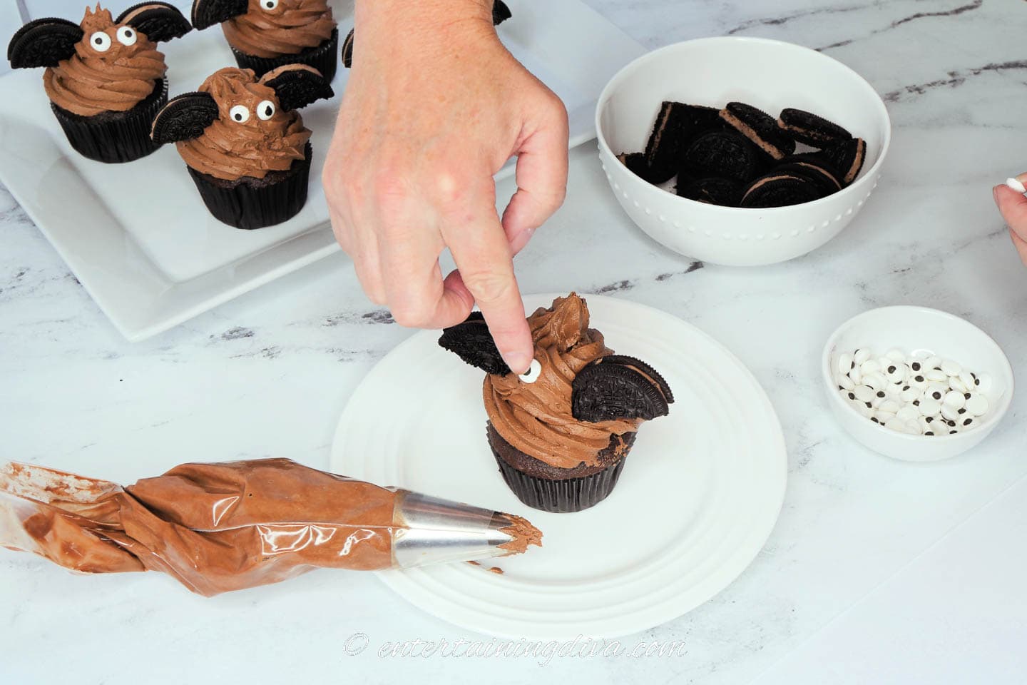 Candy eyes being stuck into the chocolate frosting between the Oreo cookie bat wings