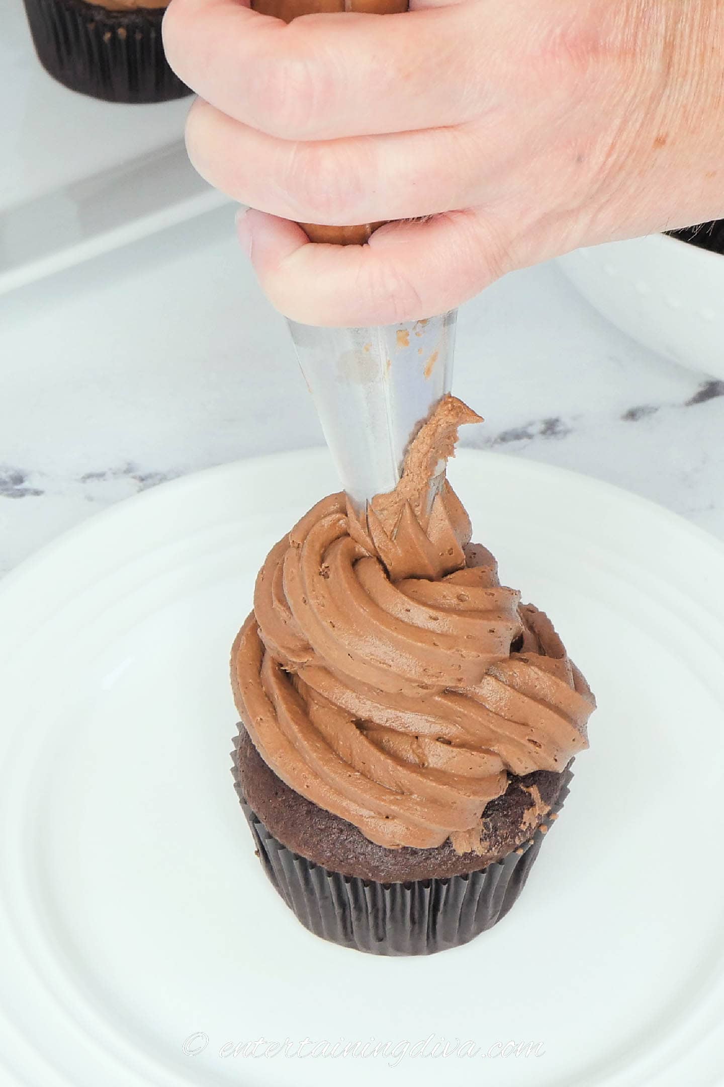 chocolate buttercream frosting being piped onto a chocolate cupcake