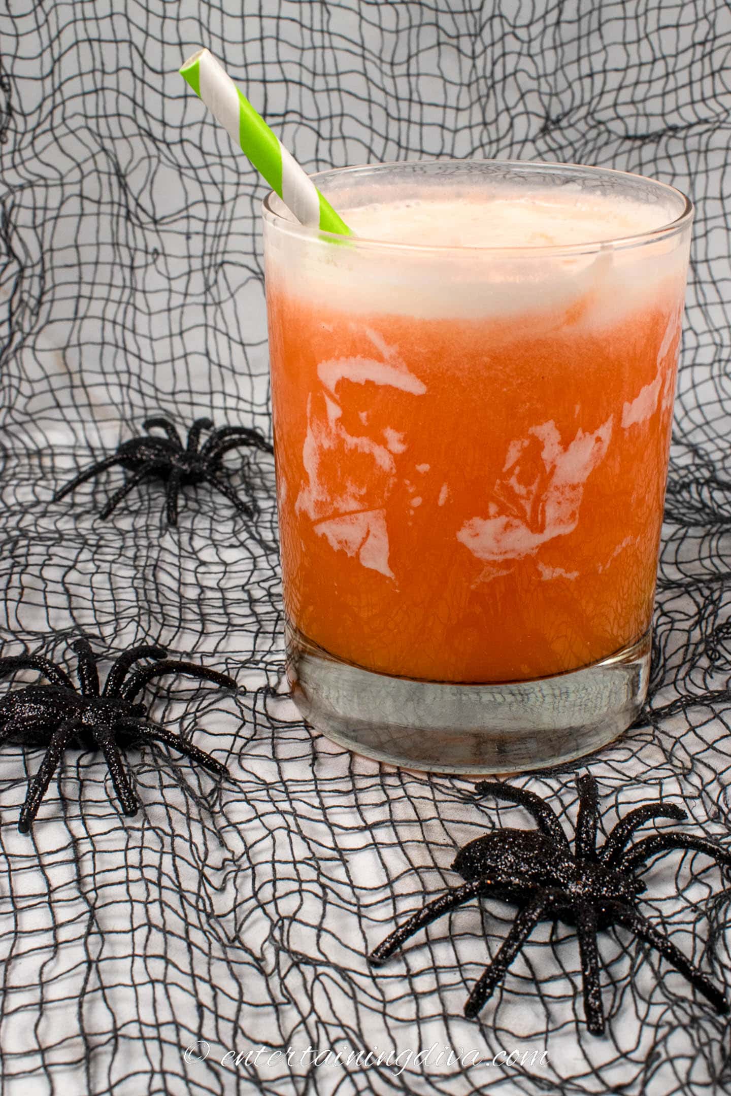 Orange creamsicle cocktail with black mesh and spiders in the background