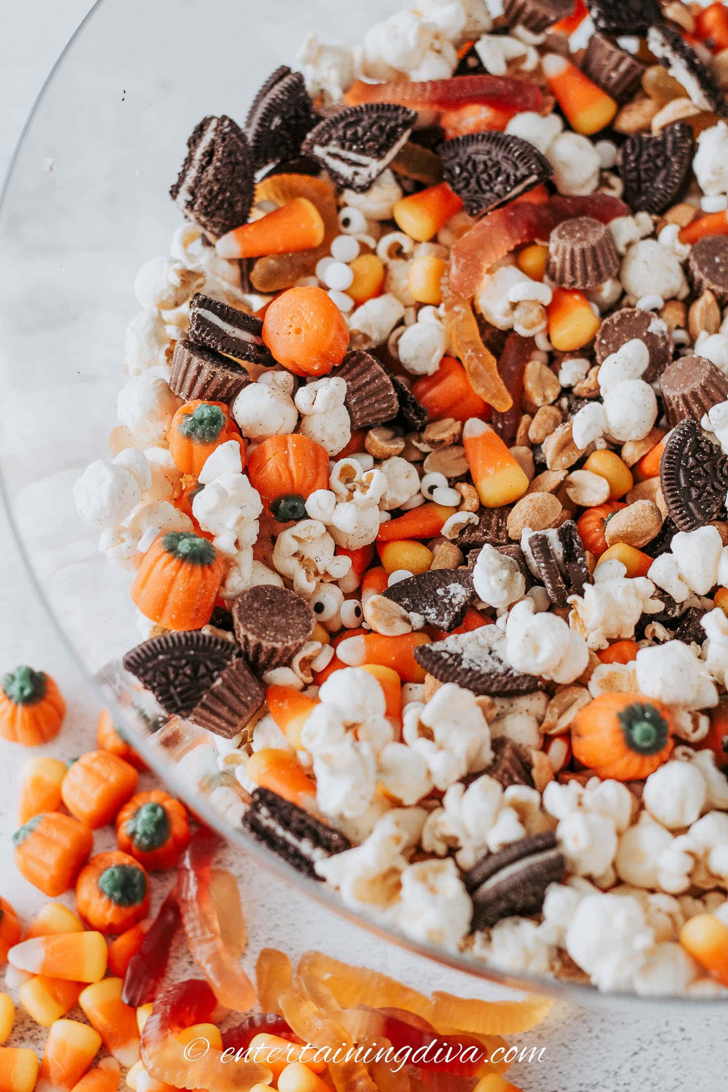A bowl of Halloween party mix with popcorn, candy corn, candy pumpkins, mini Reese's, Oreo cookies, peanuts, gummy worms and candy eyes.