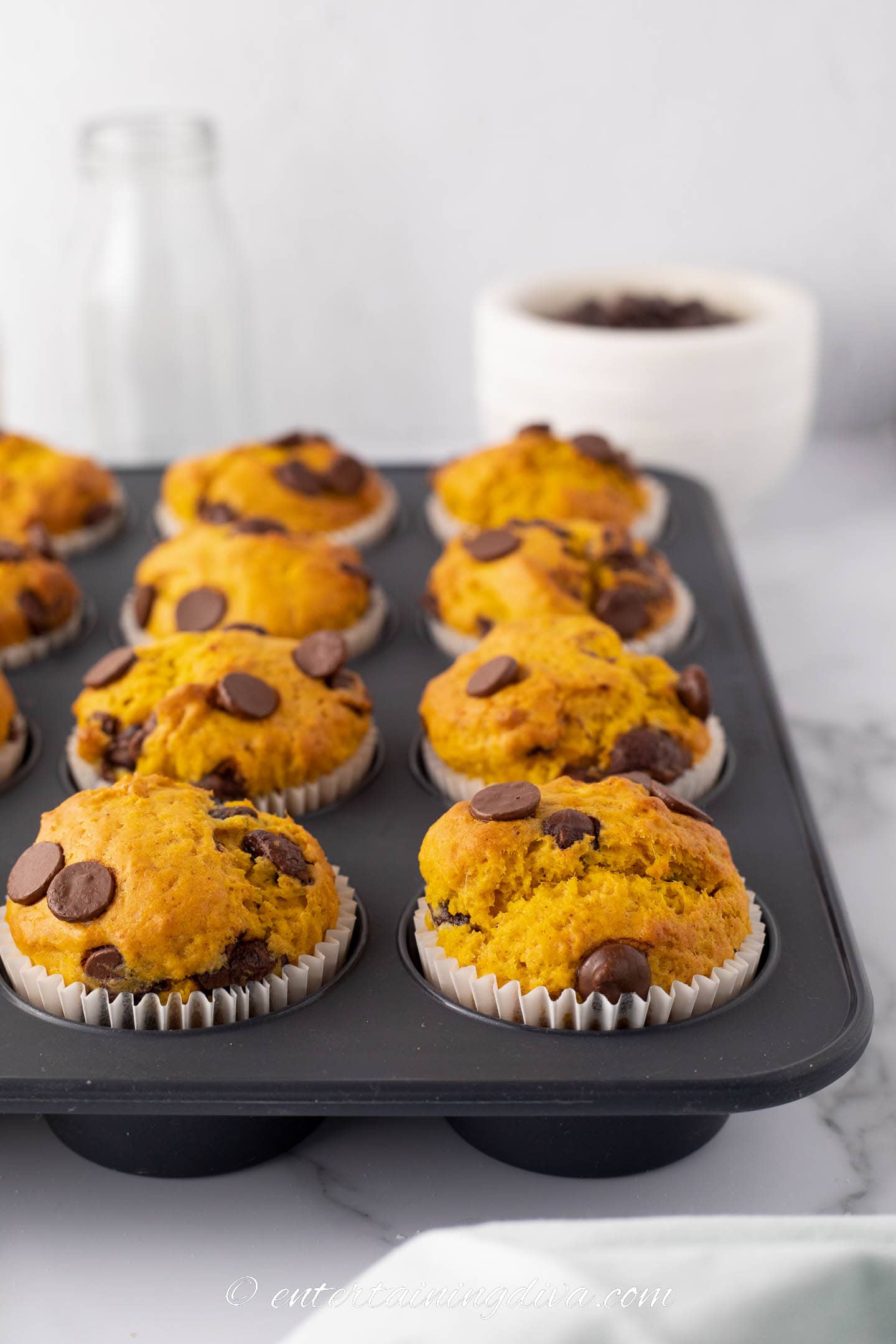 pumpkin chocolate chip muffins in a muffin tin in front of a bowl of chocolate chips