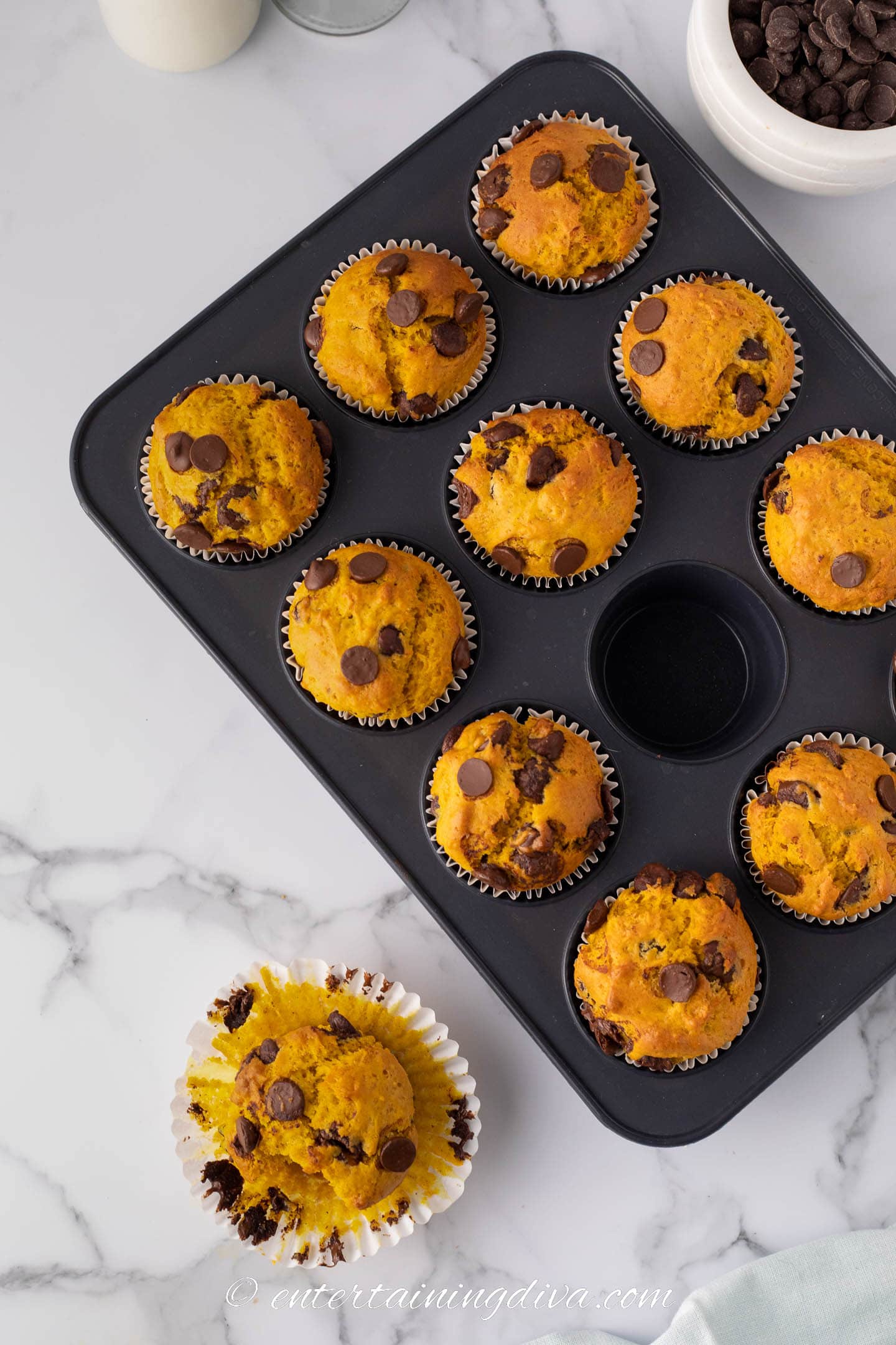 Overhead picture of a tin of pumpkin chocolate chip muffins with one out of the tin