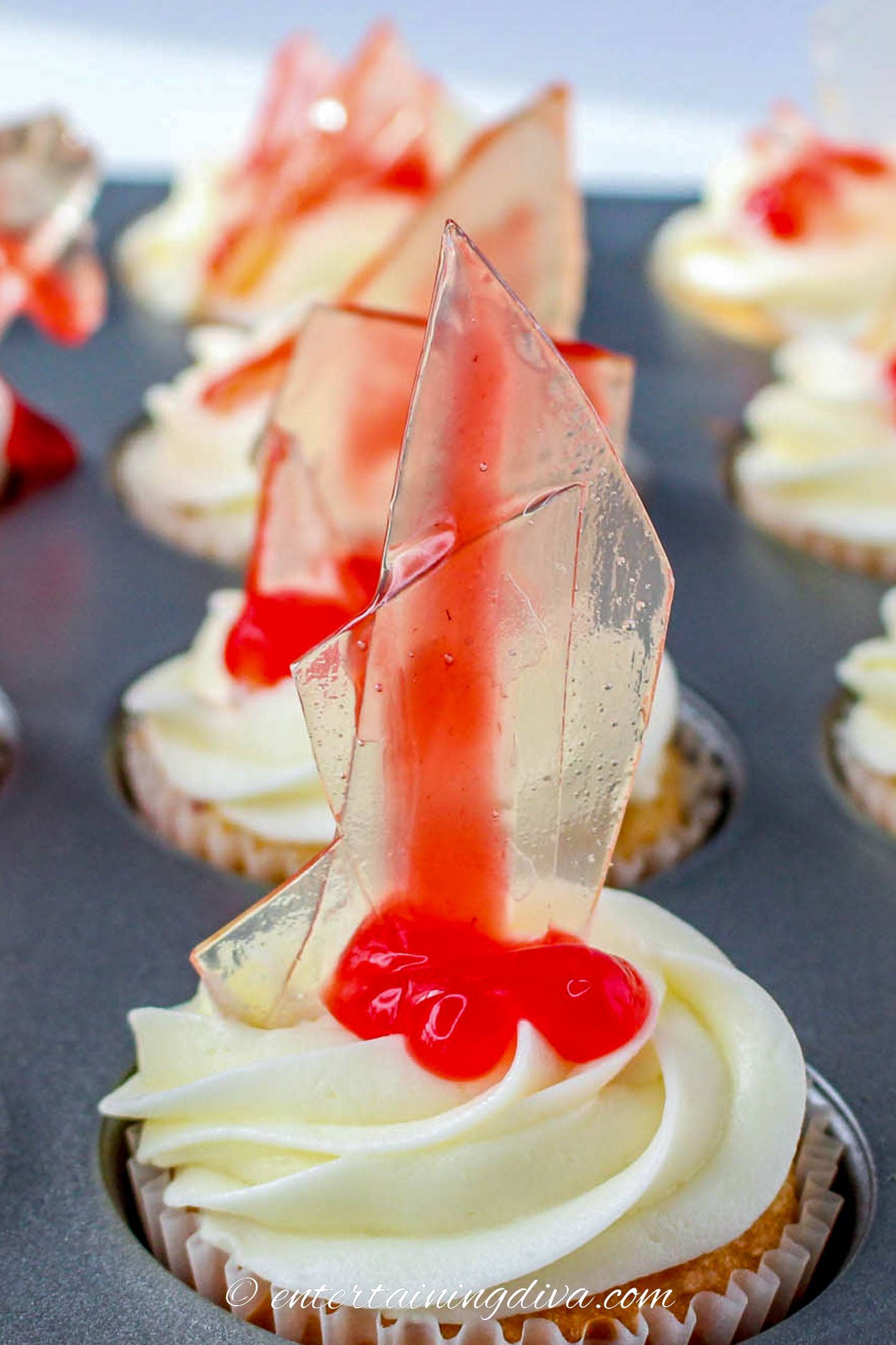 Close up of broken glass Halloween cupcake with white frosting, candy glass shard and strawberry filling blood