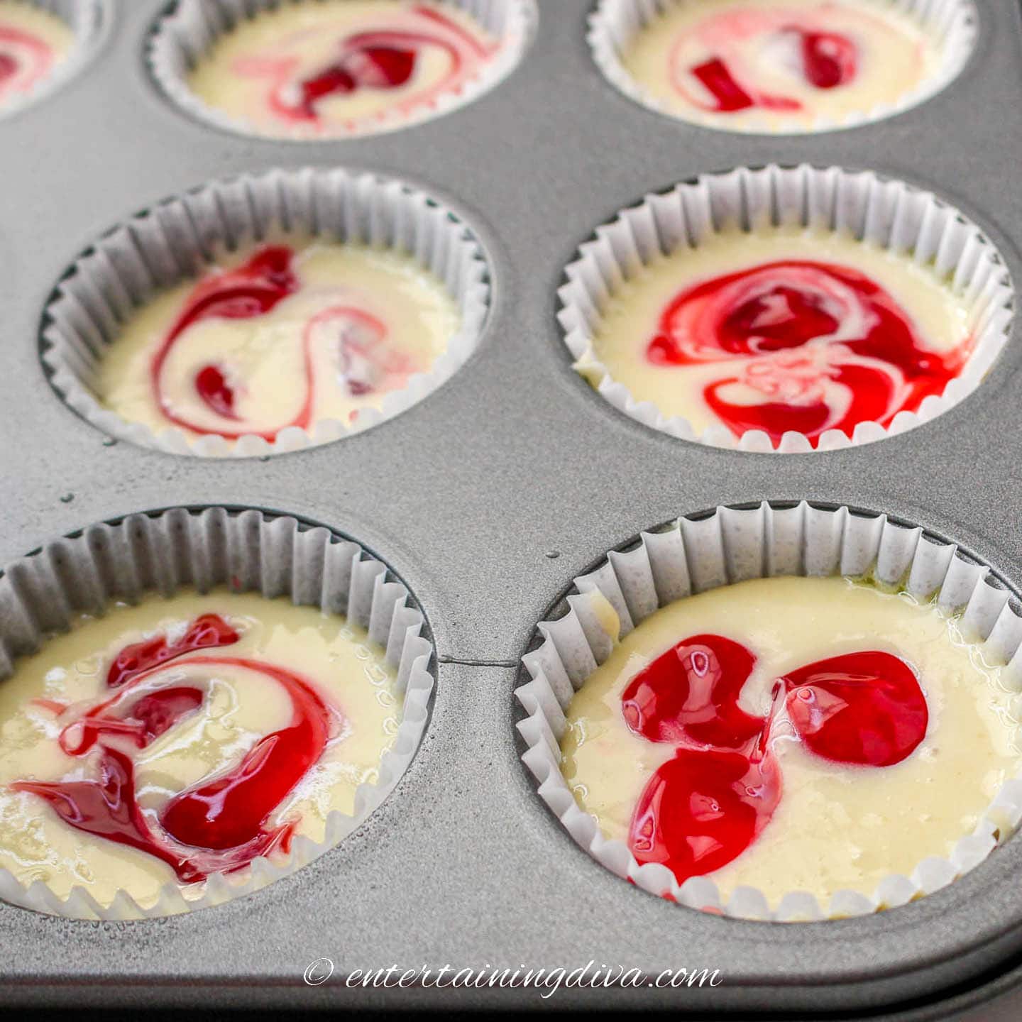 Cupcake batter in muffin tins with strawberry swirls in the top
