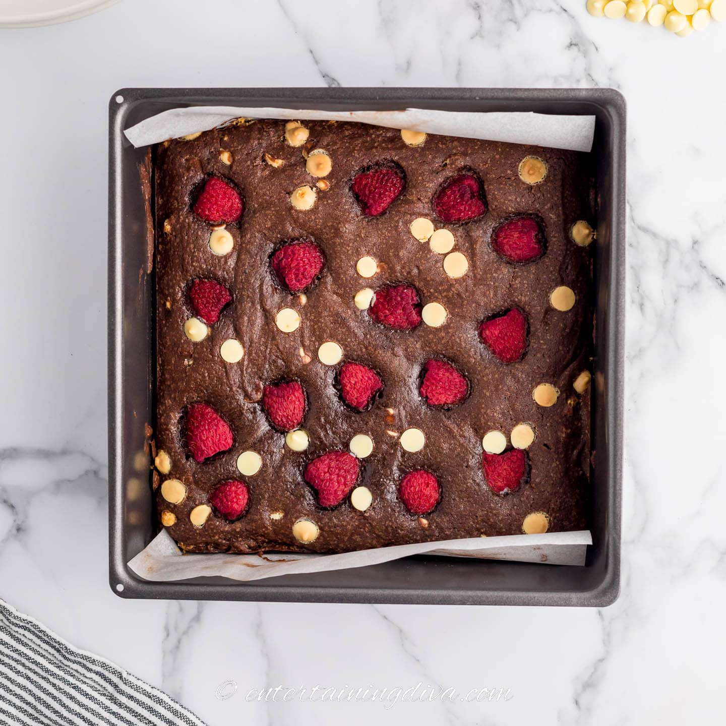Baked white chocolate raspberry brownies in a square baking tin