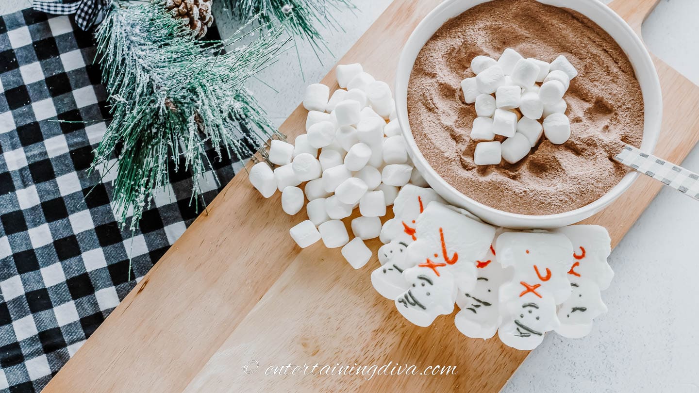 hot chocolate mix in a bowl with marshmallows and snowman peeps on a cutting board