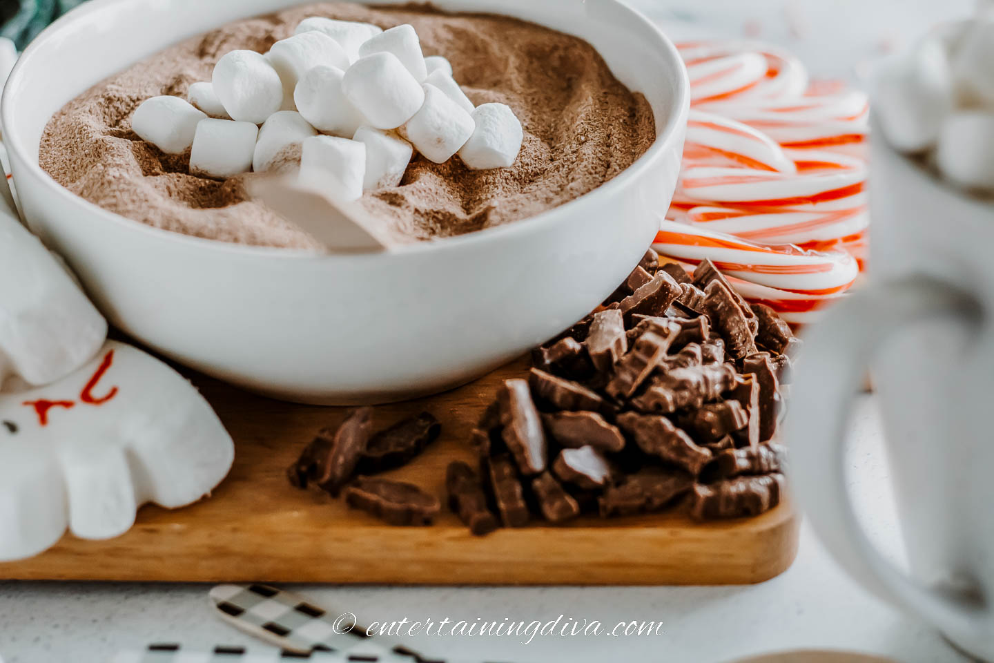 hot chocolate mix in a bowl, mini marshmallows, candy canes and chocolate on a cutting board