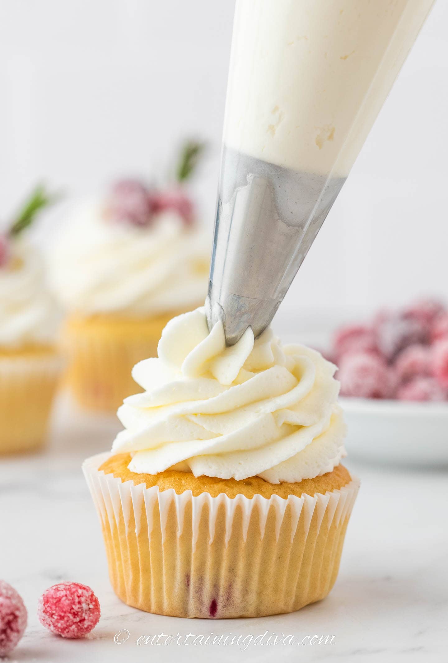 white chocolate buttercream frosting being piped onto a white chocolate cranberry cupcake