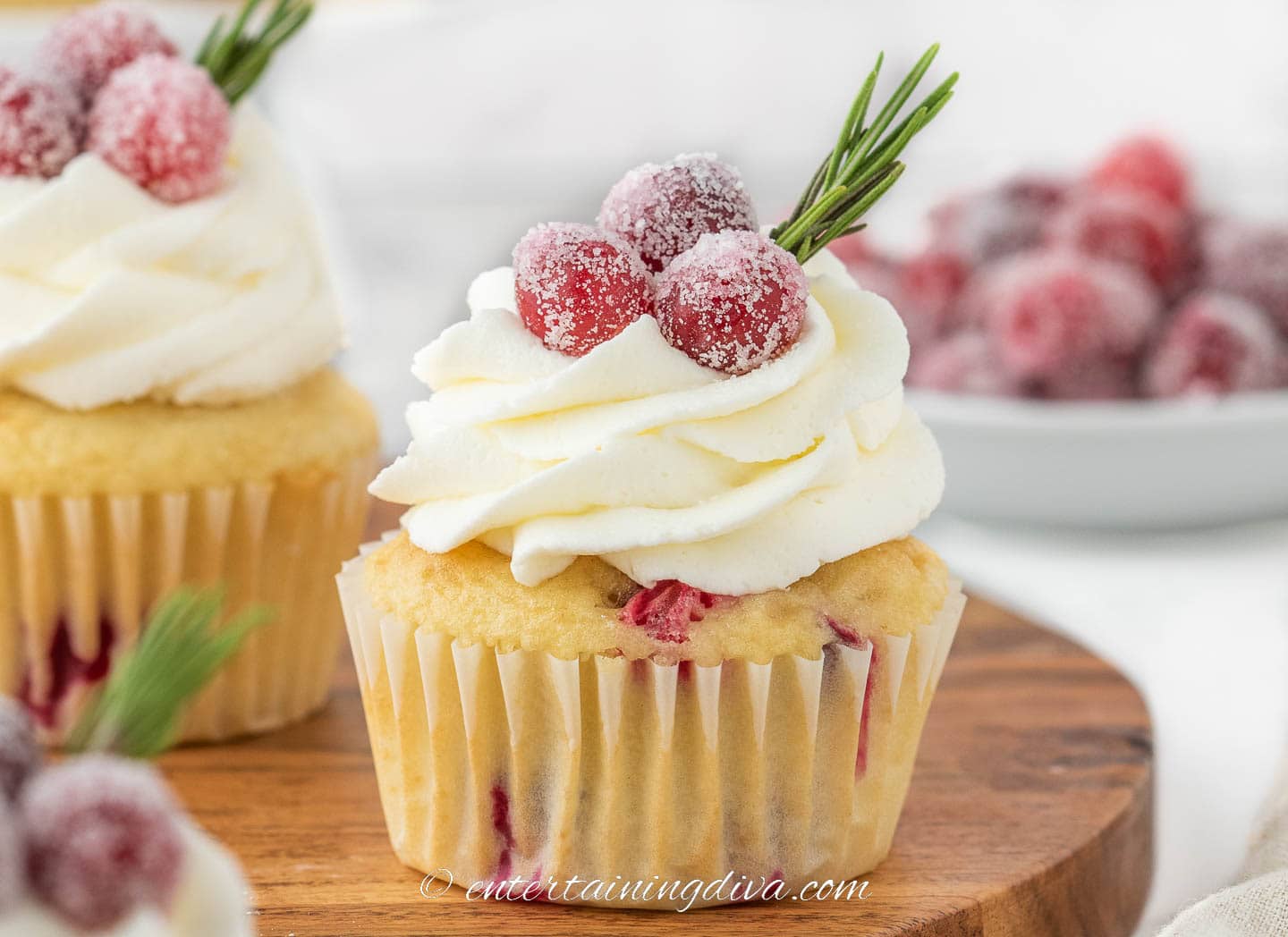 white chocolate cranberry cupcake with sugared cranberries in a bowl in the background