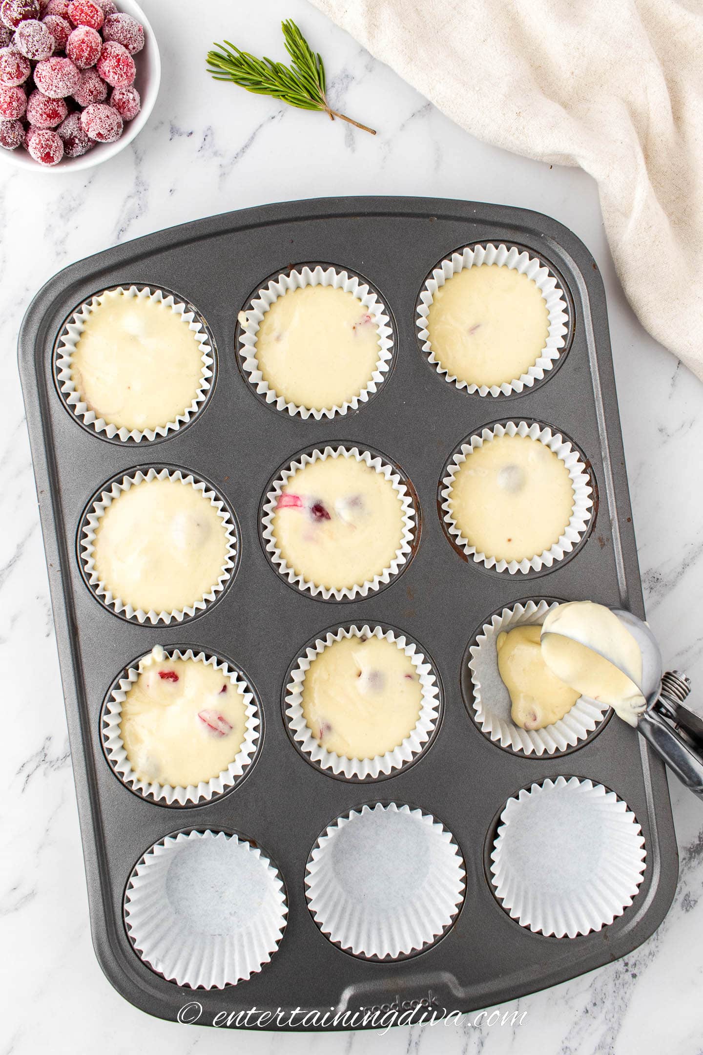 muffin tin being filled with white chocolate cranberry cupcake mixture