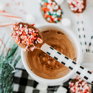 diy hot cocoa spoon dipped in chocolate with crushed candy canes on top of a mug of hot chocolate