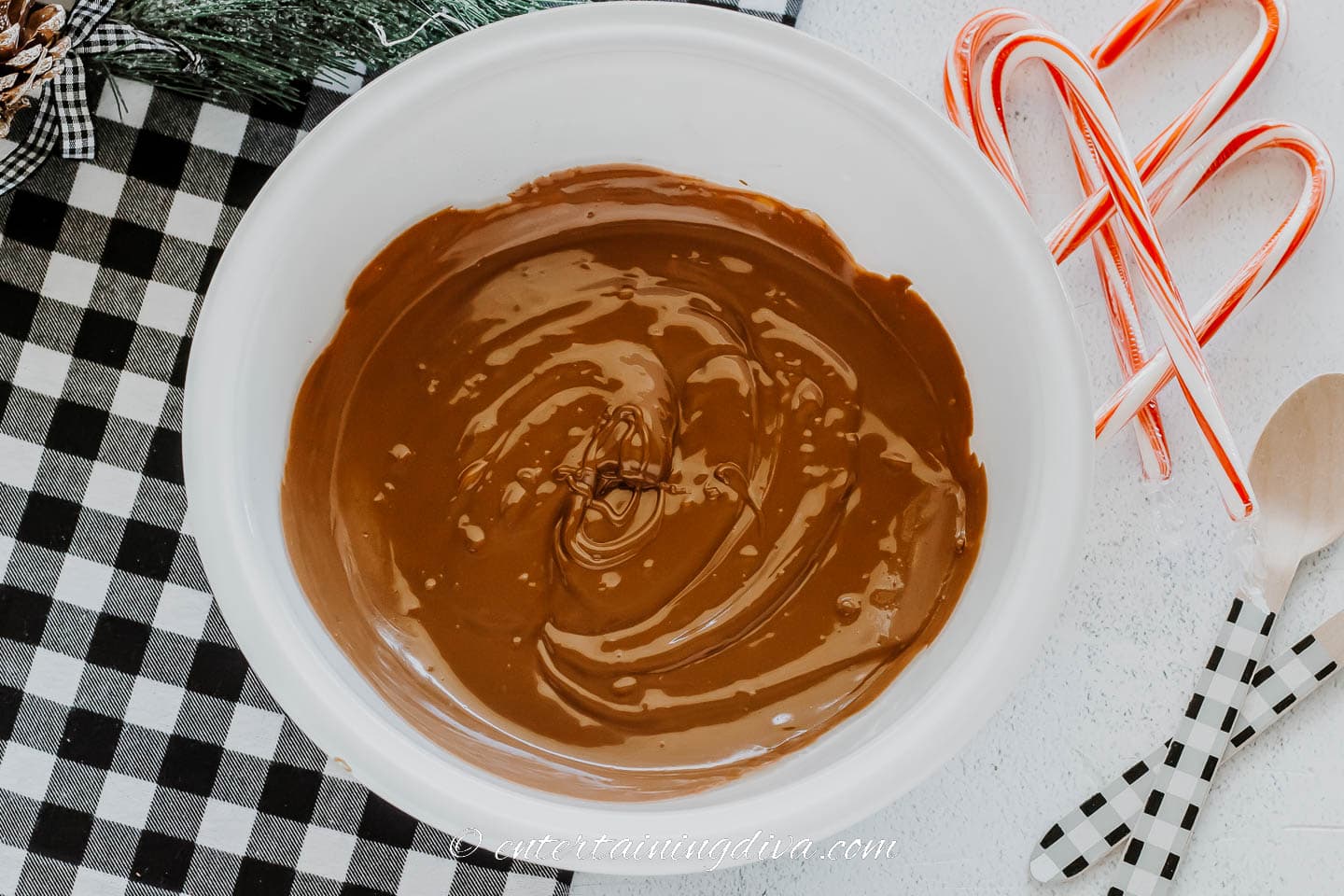 Melted chocolate in a bowl beside candy canes and disposable wooden spoons