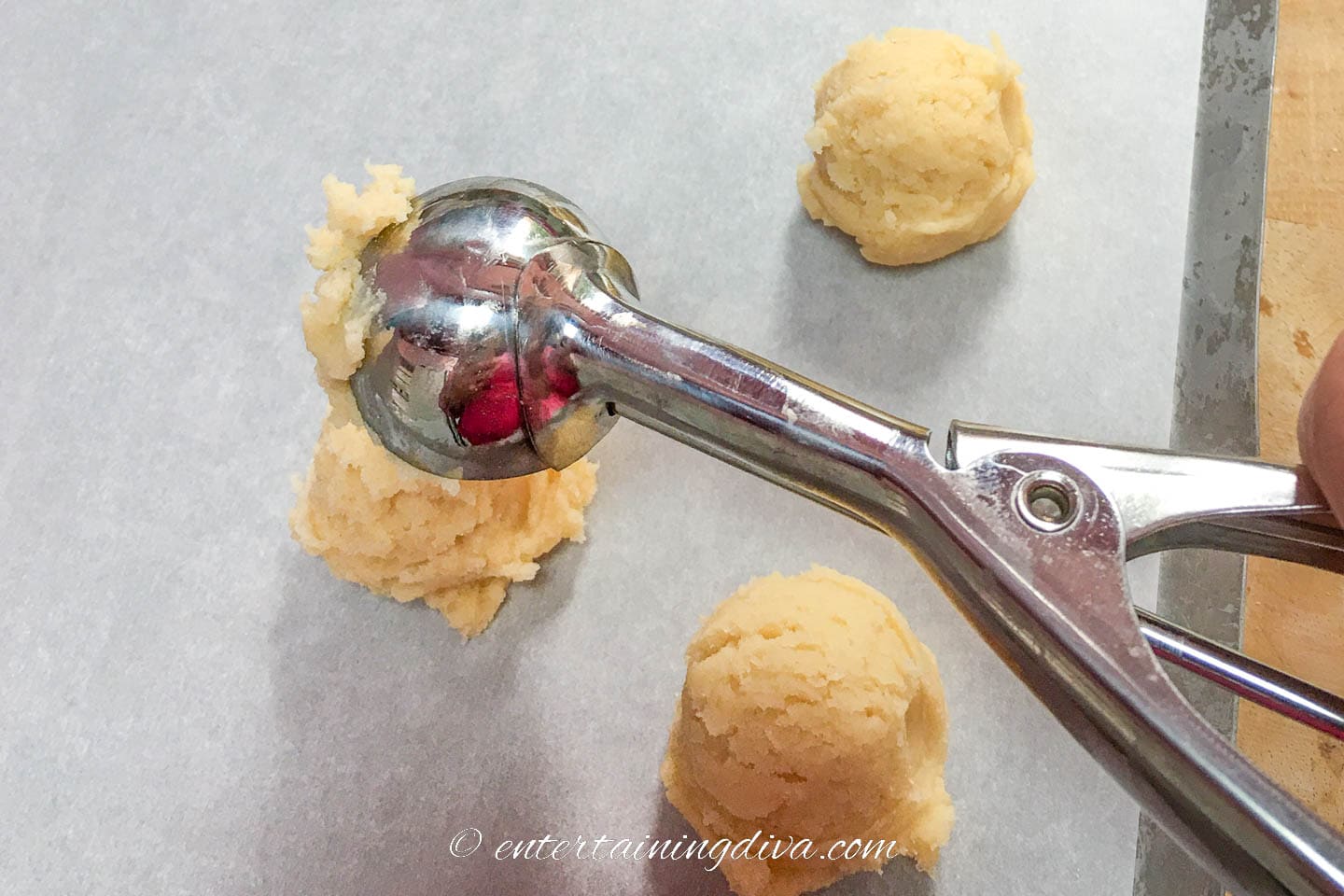 cookie dough being dropped onto a baking sheet with an ice cream scoop