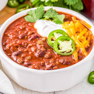 thick chili in a bowl garnished with jalapeno peppers, sour cream and grated cheese