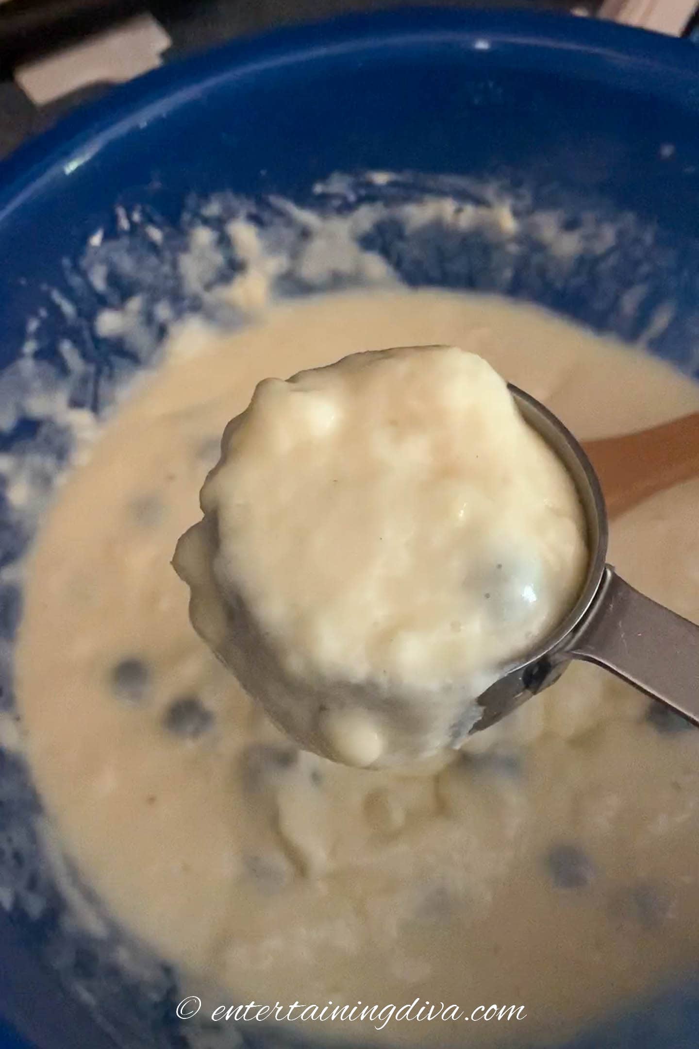 Pancake batter being scooped out of the bowl with a measuring cup