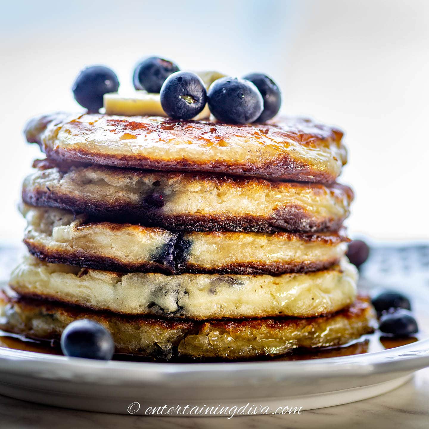 side view of a stack of blueberry pancakes served with maple syrup and fresh blueberries