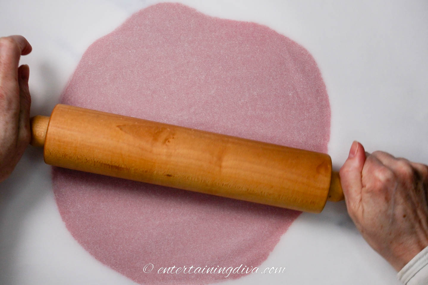 Red cookie dough being rolled out by a rolling pin