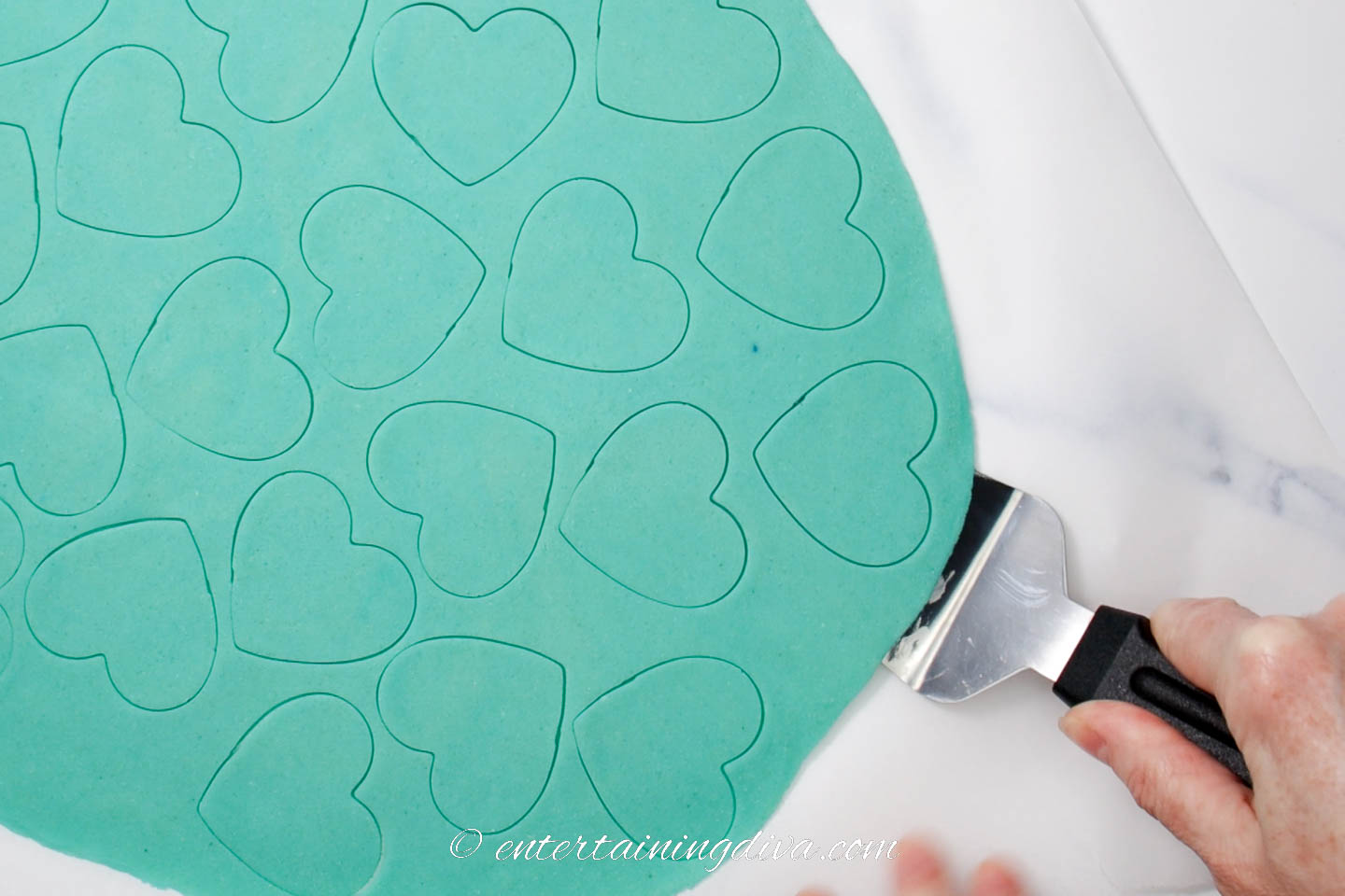 Heart cut outs being removed from the rolled out cookie dough