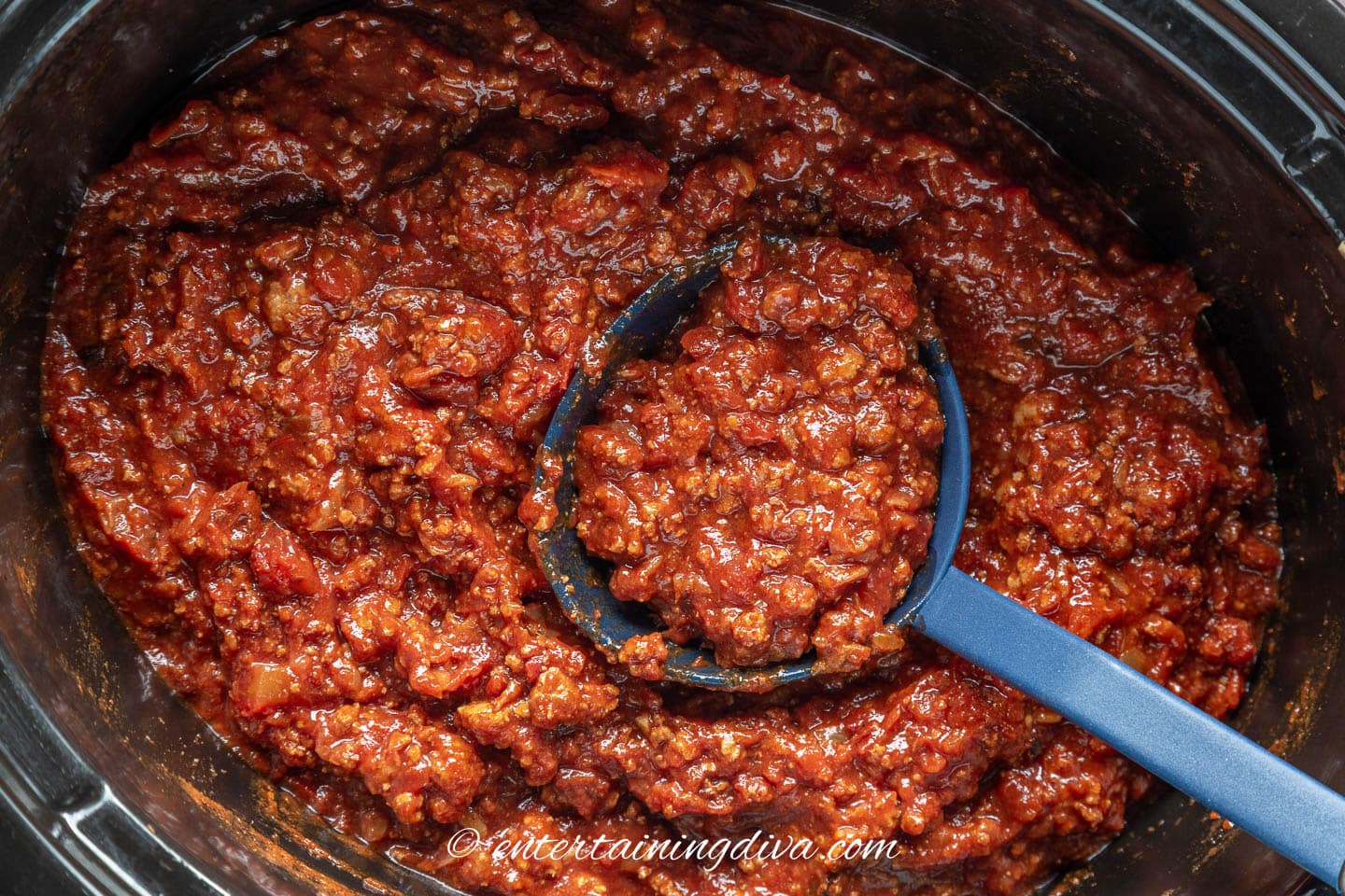 A spoon with no bean chili in a slow cooker