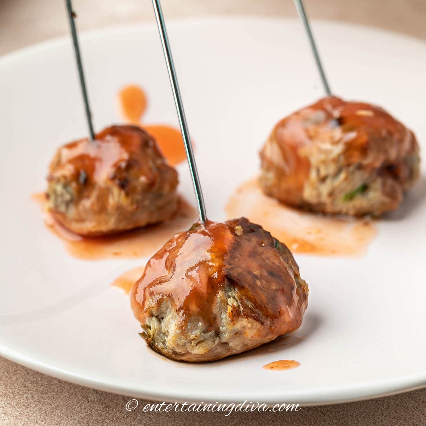 Sweet and sour meatballs on a plate with metal toothpicks