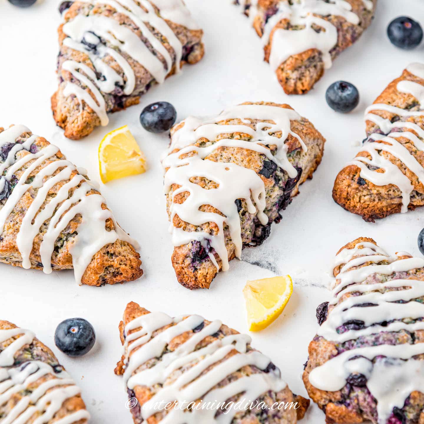 glazed lemon blueberry scones on a counter with slices of lemon and fresh blueberries