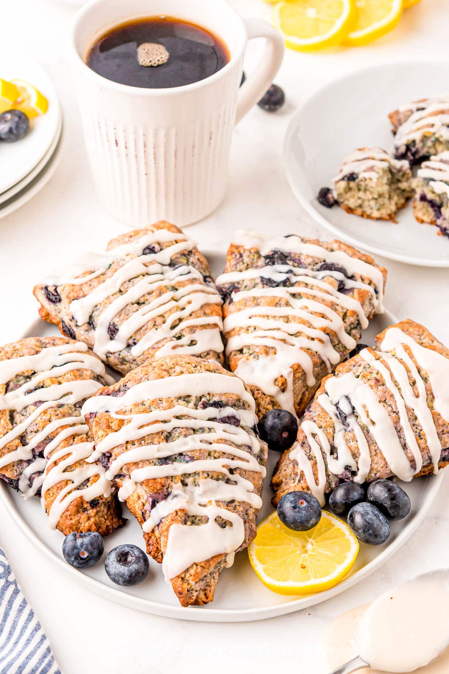 glazed lemon blueberry scones on a plate with a cup of coffee behind them