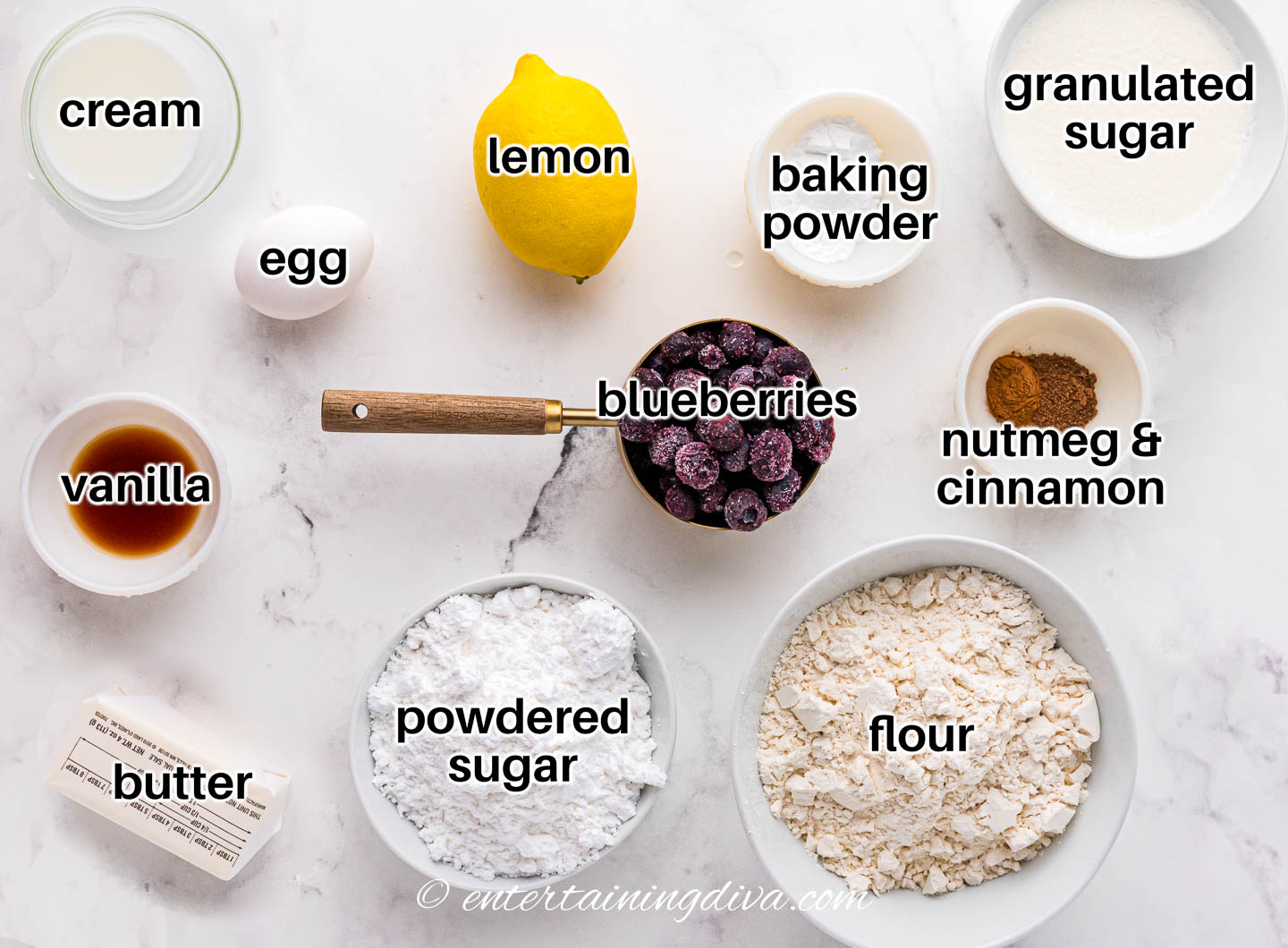 ingredients for lemon blueberry scones (frozen blueberries, lemon, sugar, baking powder, nutmeg, cinnamon, flour, egg, butter, vanilla) and glaze (powdered sugar, vanilla, cream)